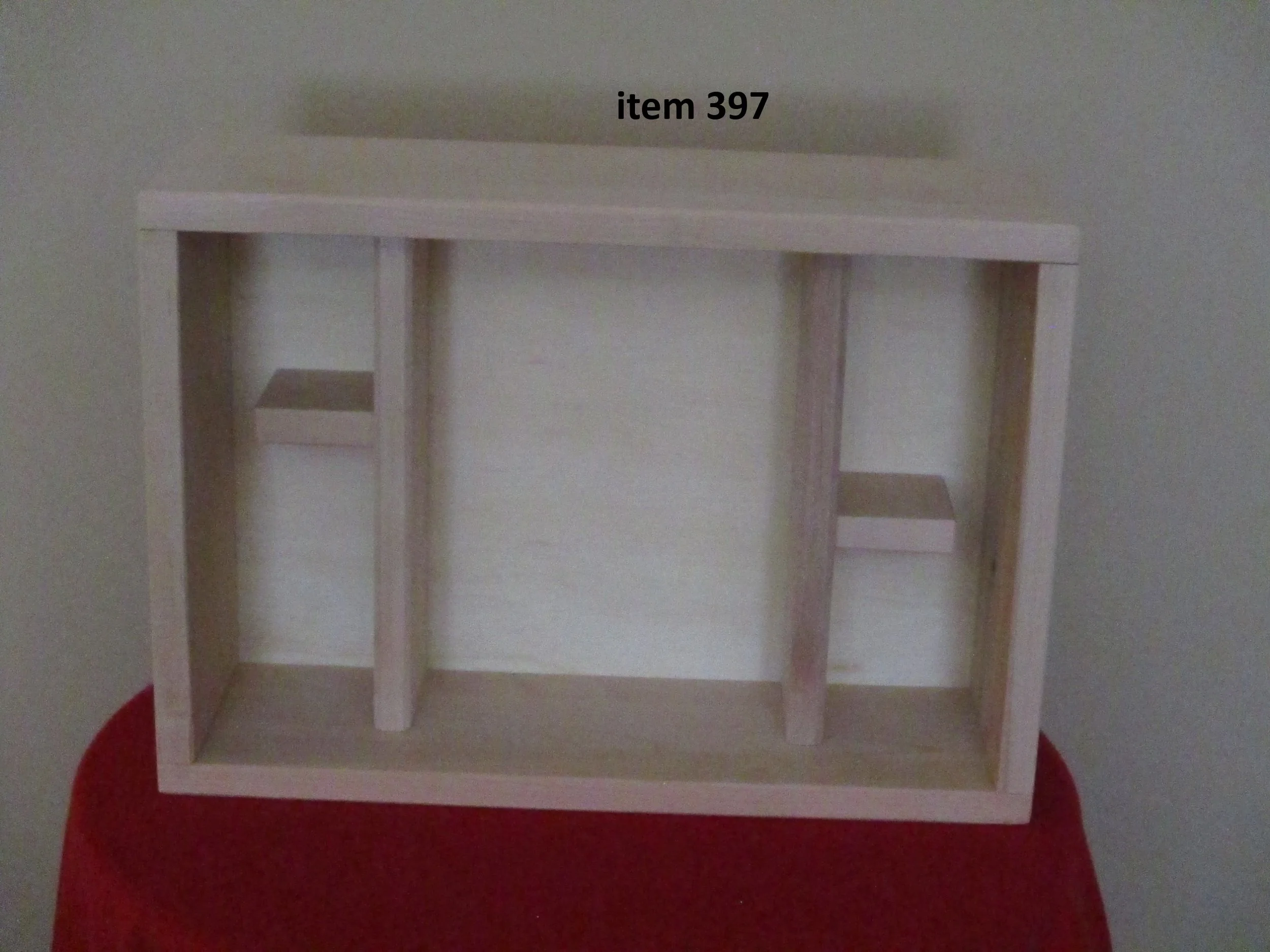 Empty wooden miniature house or furniture frame with item number 397 written above it, placed on a red cloth background.