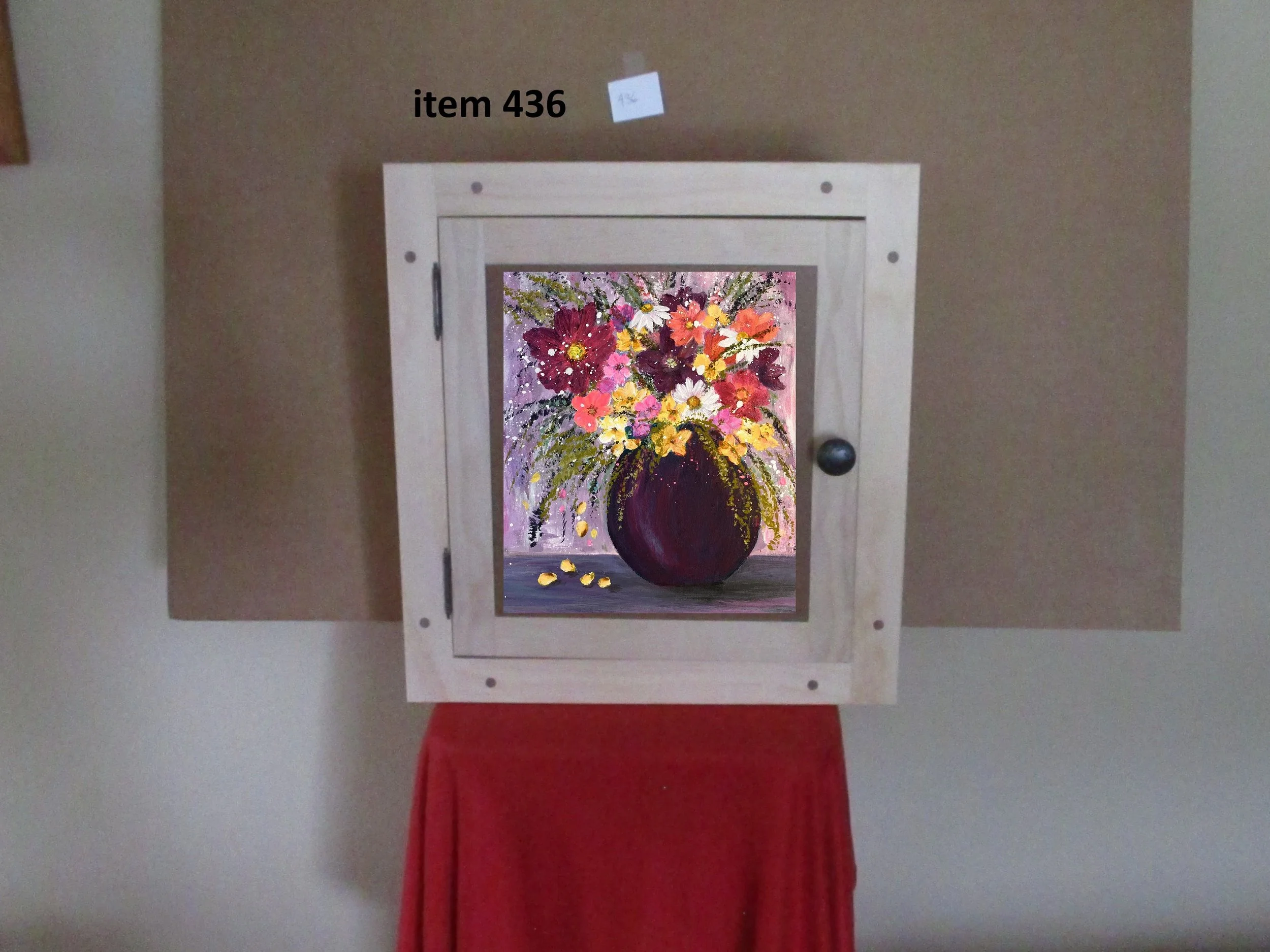 Painting of a colorful floral bouquet in a dark purple vase, displayed behind a small window on a wooden wall.