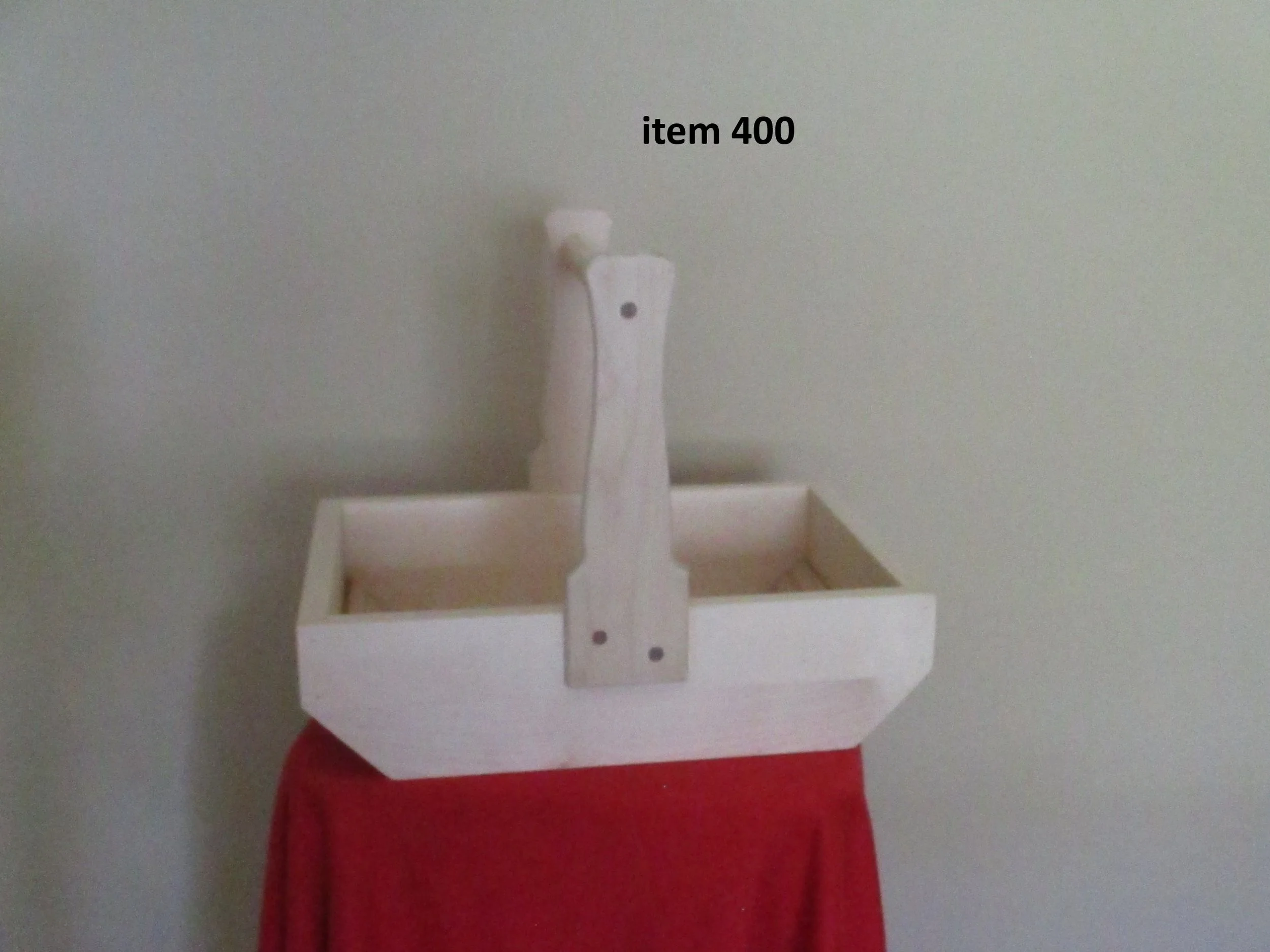 A wooden structure resembling a small boat with a vertical mast, placed on a red fabric-covered surface against a plain wall. The boat is made of light-colored wood and has an open top. The mast is attached at the front of the boat, labeled 'item 400.'