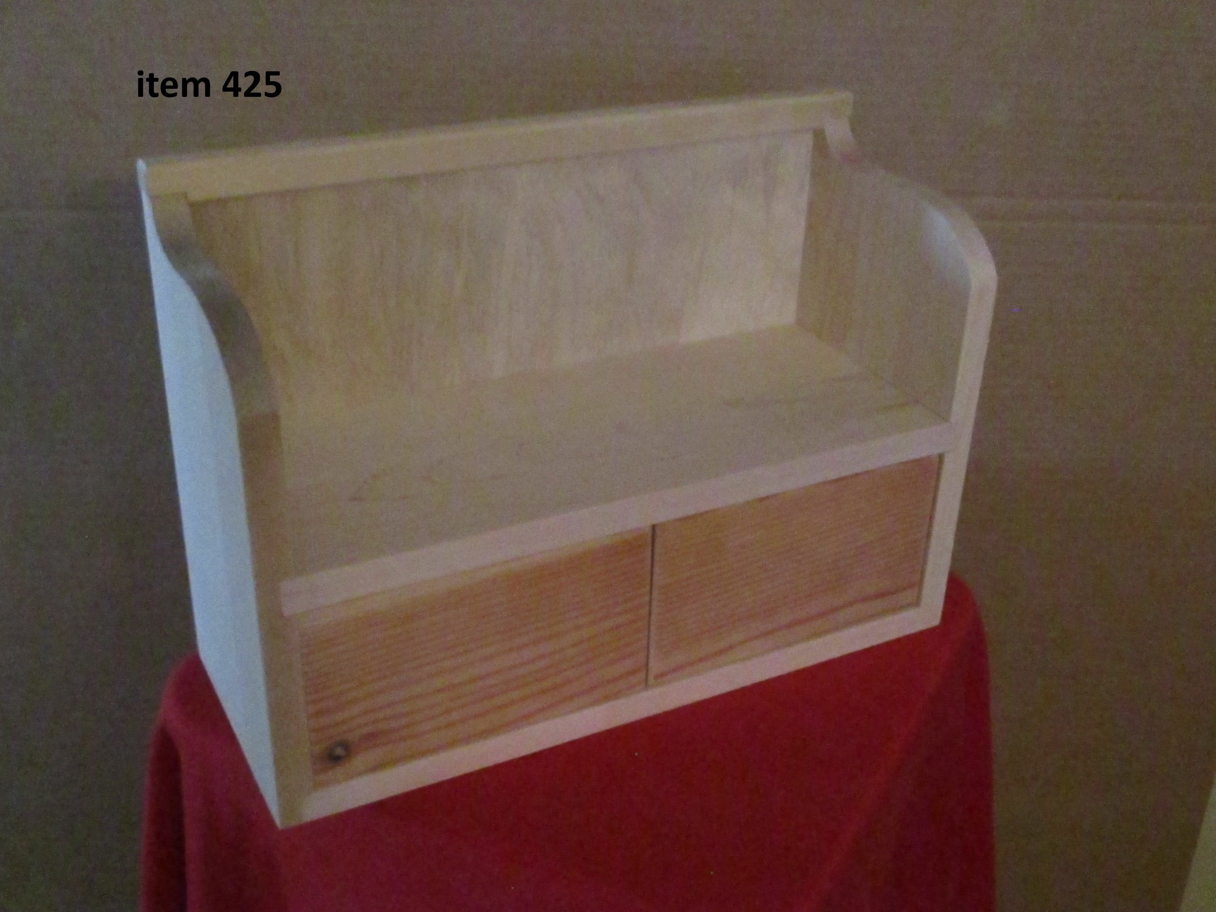 A wooden display cabinet with a back panel and sliding doors, placed on a red cloth-covered surface.
