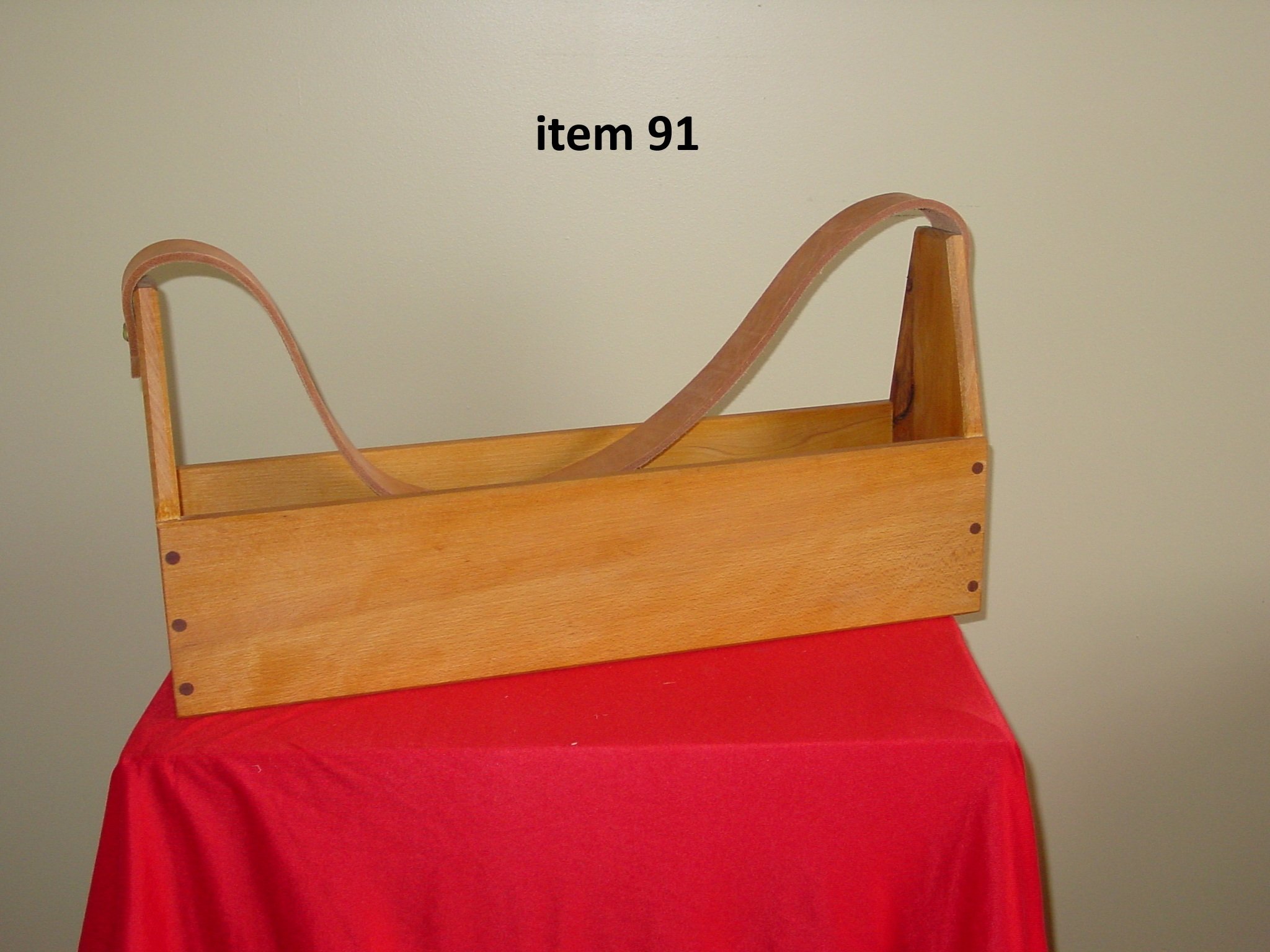 A wooden sled with a curved handlebar sitting on a red cloth with a plain beige wall in the background, labeled 'item 91'.