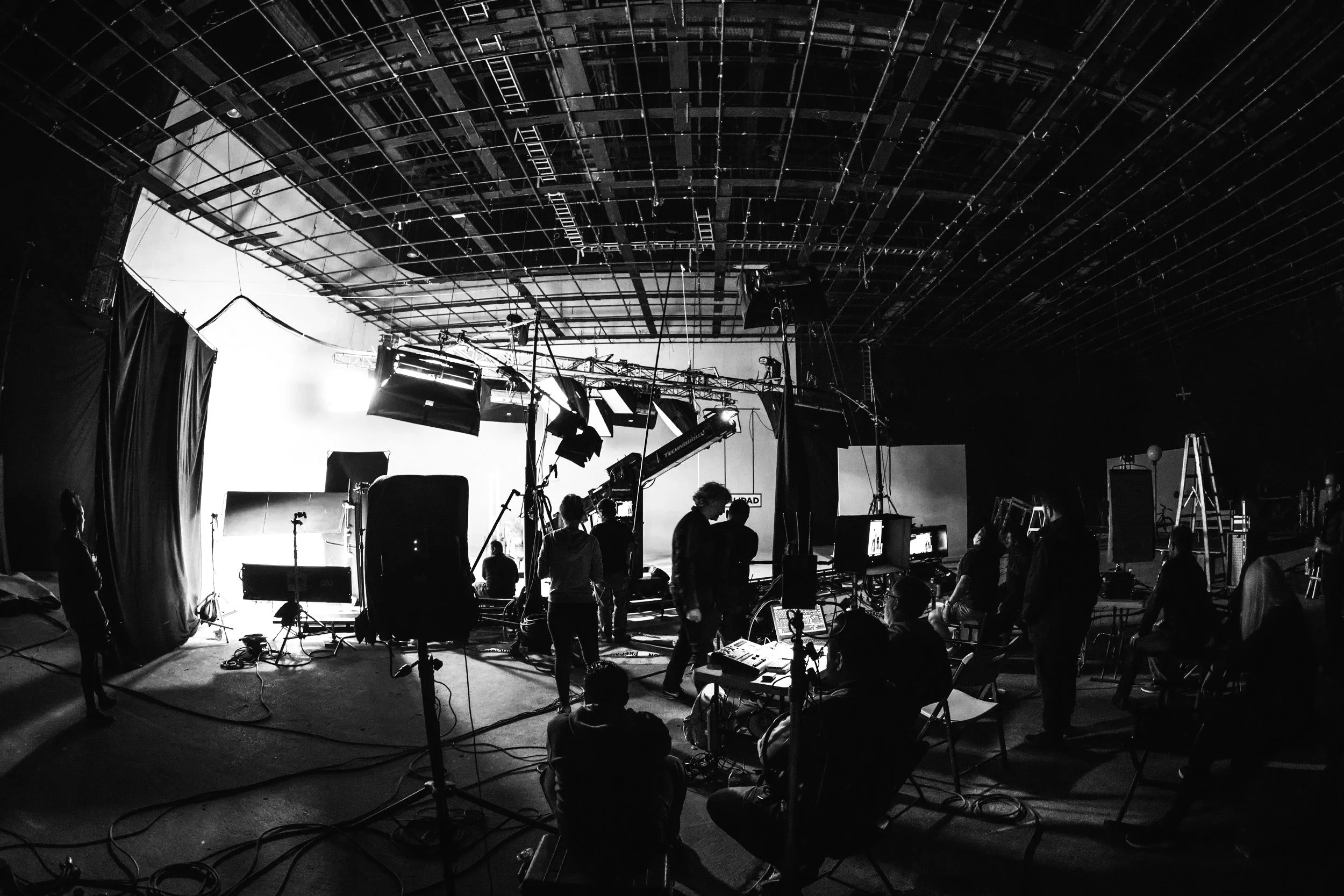 Behind-the-scenes view of a film or TV production set with crew members, cameras, and lighting equipment.