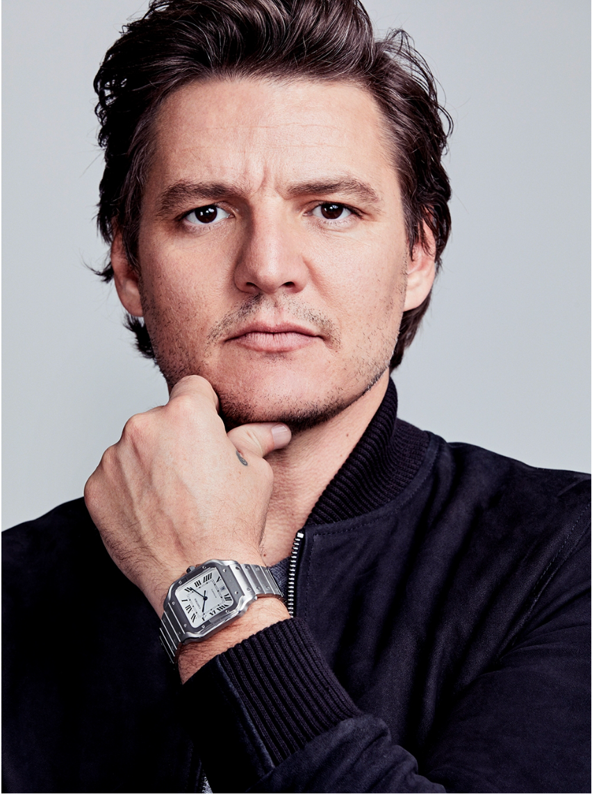 A man with dark hair, wearing a black jacket, staring directly at the camera with his hand resting on his chin, wearing a silver wristwatch.