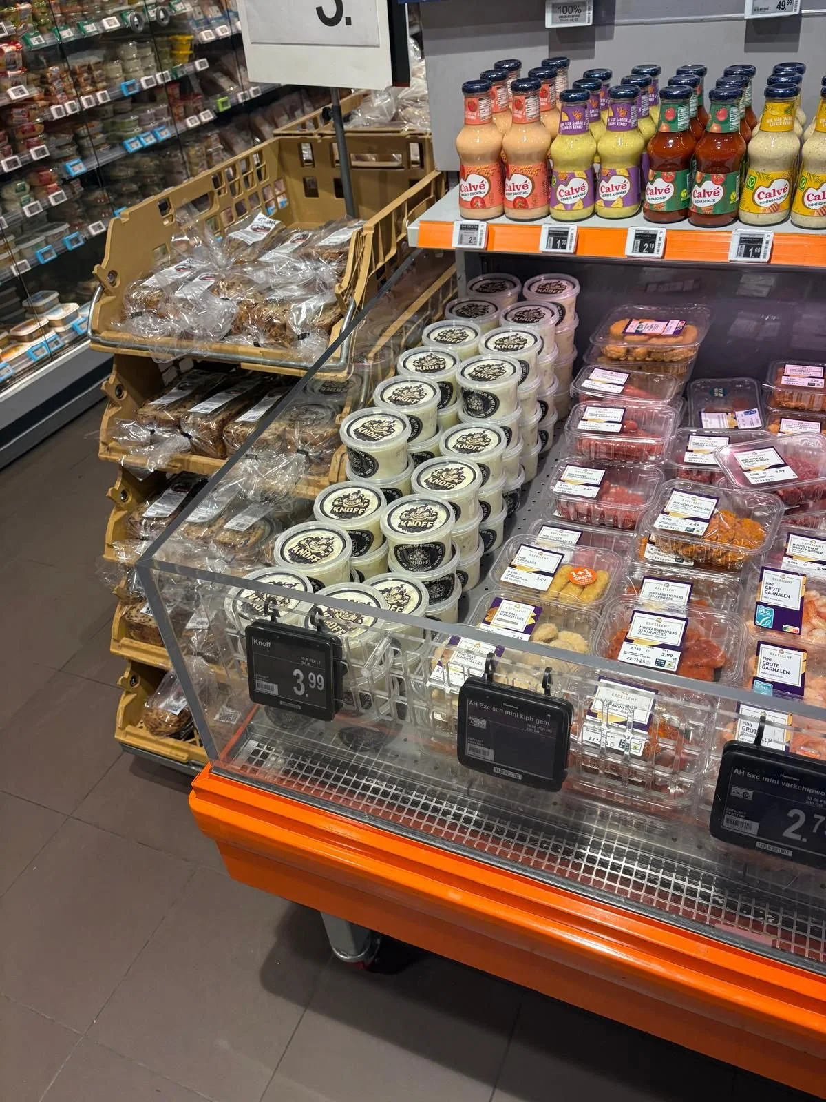 Knoff in de winkelschap. Verschillende soorten kaas en knoflooksaus in een supermarkt, met prijzen en verpakkingen zichtbaar.