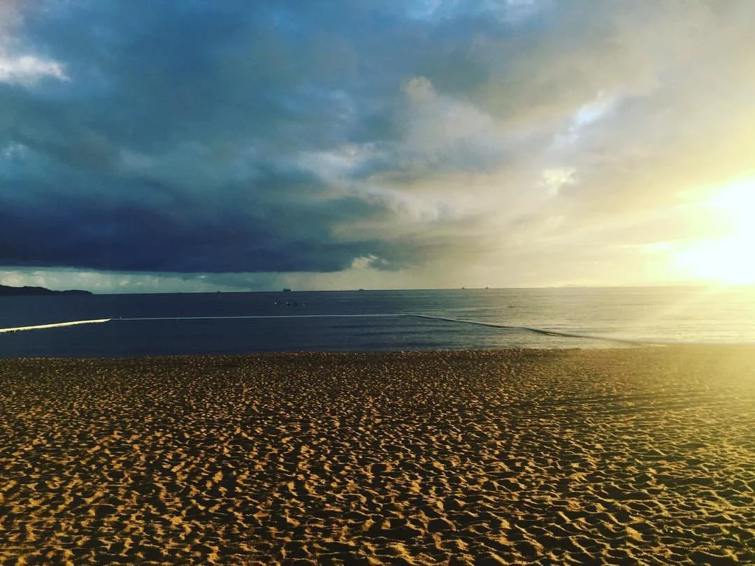 A beach scene at sunset with dark clouds over the ocean and sandy shore in the foreground.