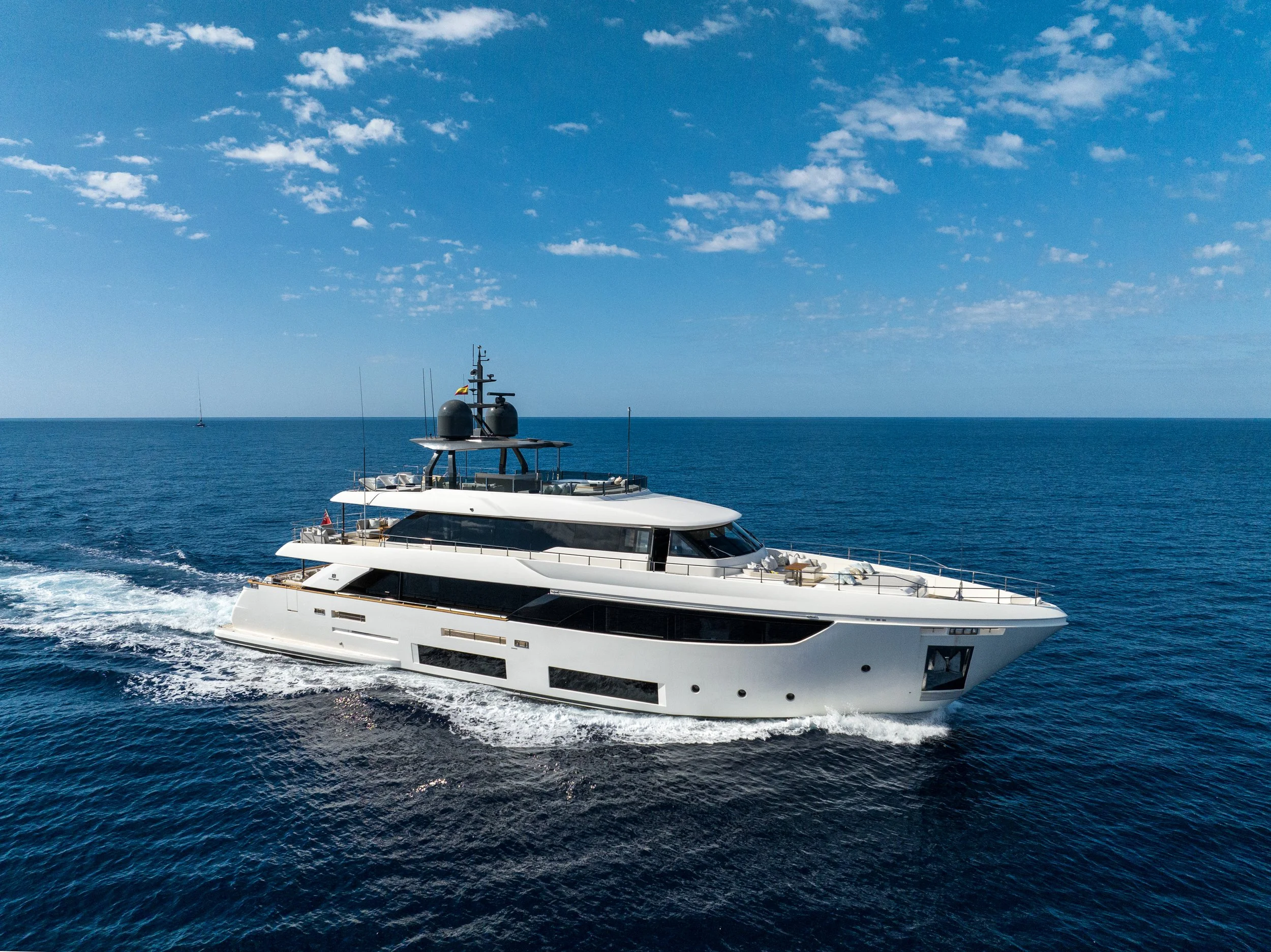 A large white yacht sailing in the ocean under a blue sky with scattered clouds.