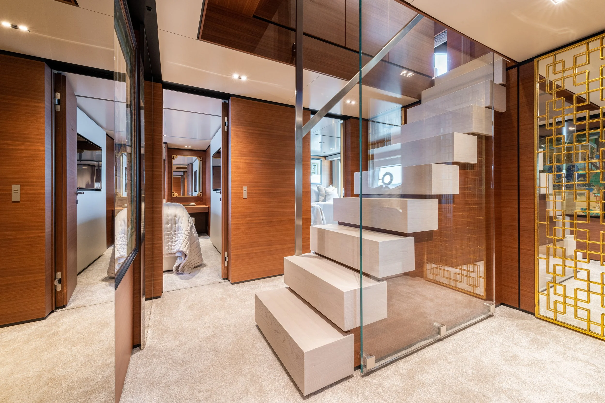 Modern interior with a glass staircase, wooden wall panels, bedrooms with white bedding, and a decorative golden partition.