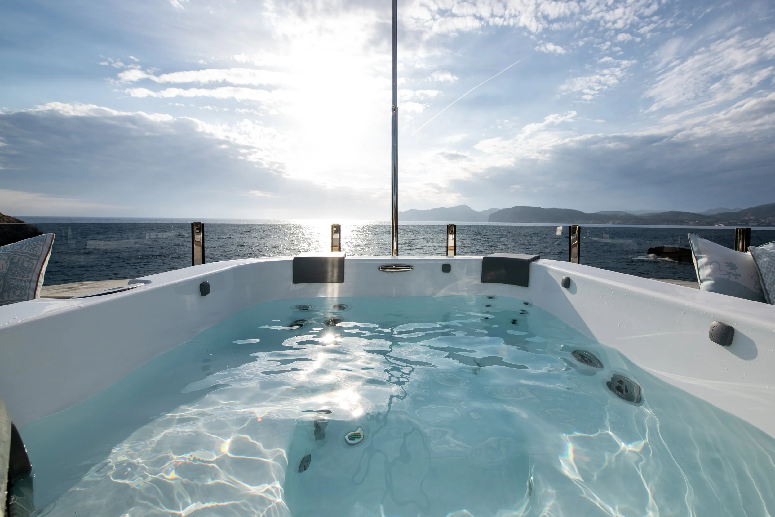 A luxurious hot tub on a yacht with a view of the ocean and distant mountains under a partly cloudy sky.