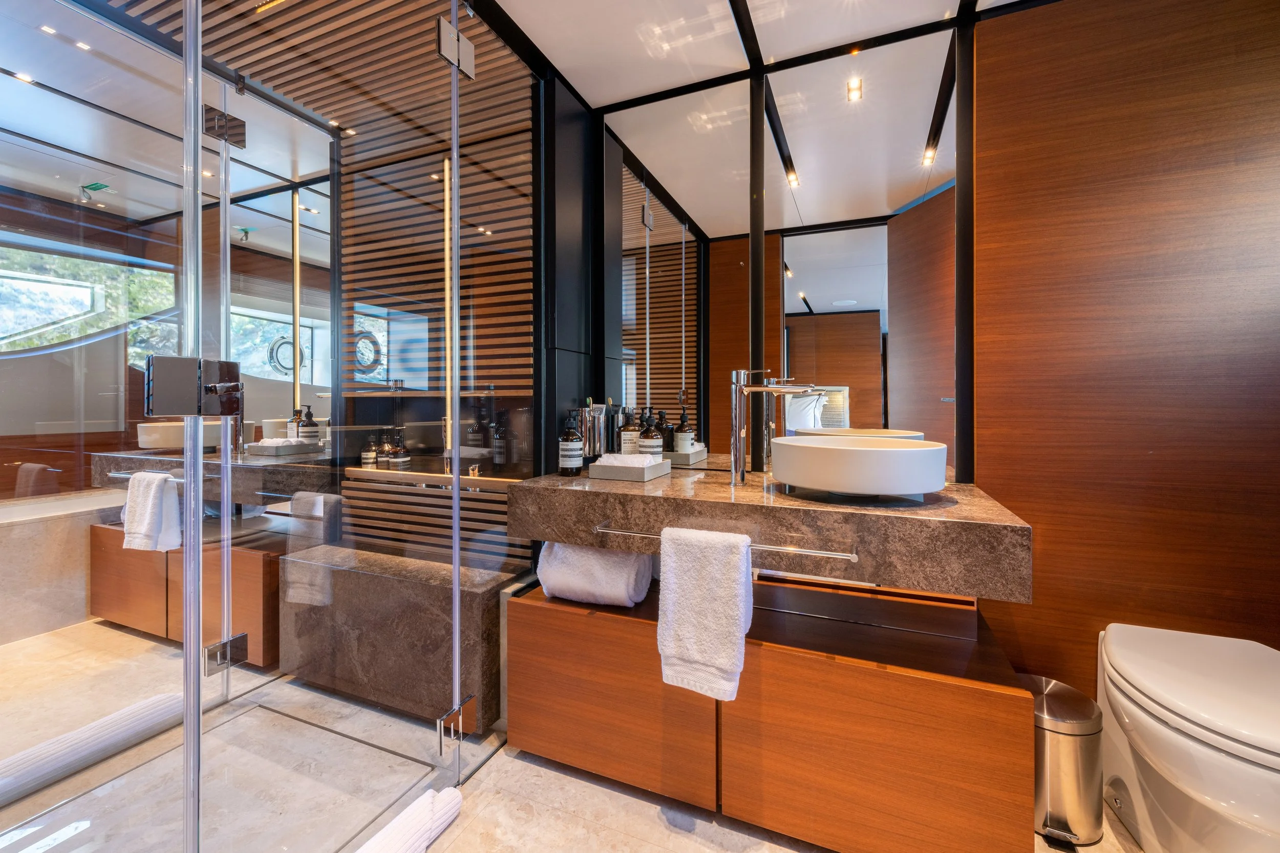 Modern bathroom with a glass shower, wooden cabinets, a marble countertop, white vessel sinks, and a mirror.