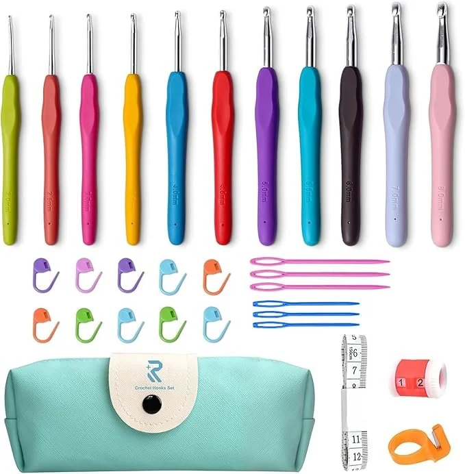 A set of colorful crochet hooks, stitch markers, sewing needles, and measuring tape arranged on a white surface with a teal carrying case.