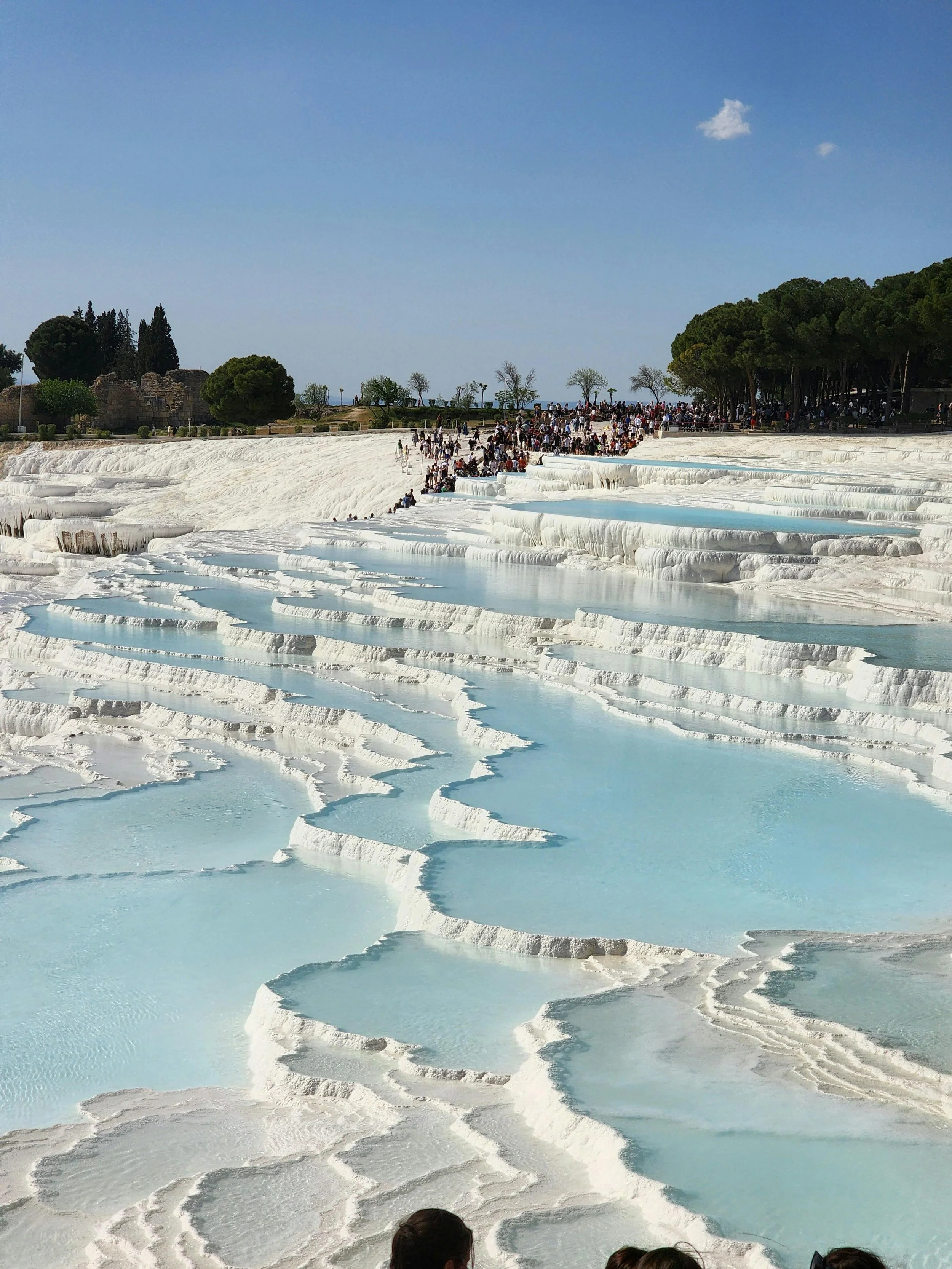 Tourists at Pamukkale's terraced mineral-rich thermal hot springs with white calcite terraces and blue pools in Turkey, under a clear sky.