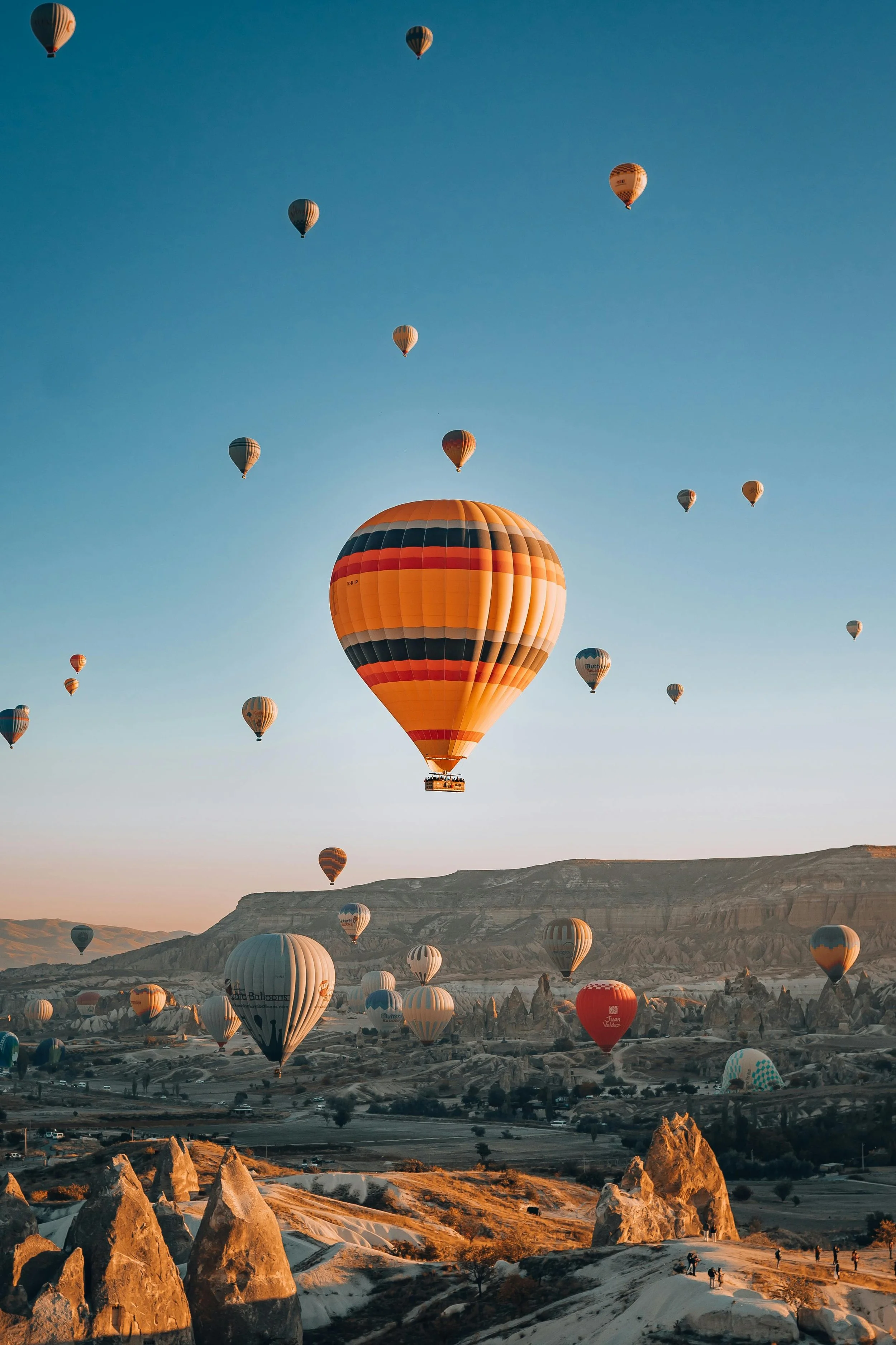 Multiple hot air balloons floating in the sky over a rocky landscape during sunrise or sunset.