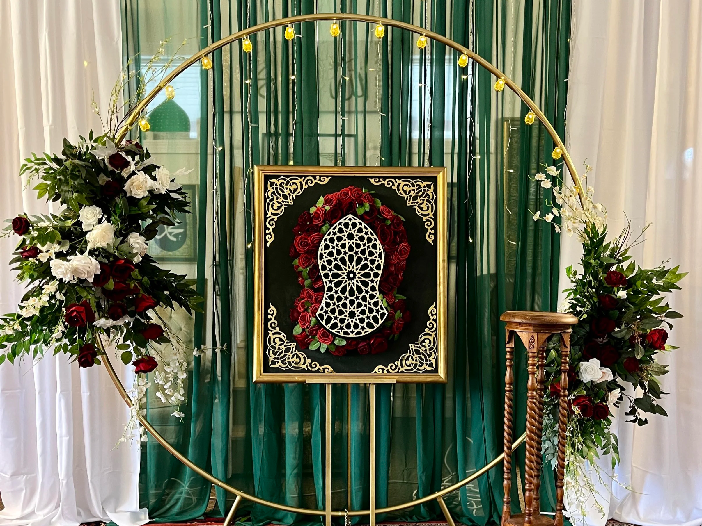 Decorative display with floral arrangements, green and white curtains, and intricate artwork framed with roses and gold accents.