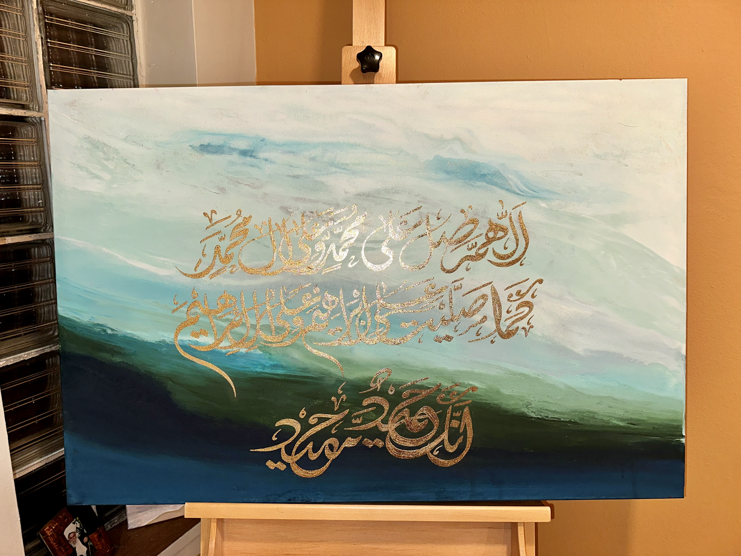 A painting with a background of watercolor-like pastel shades of sky blue, teal, light green, and dark blue, featuring gold Arabic calligraphy.