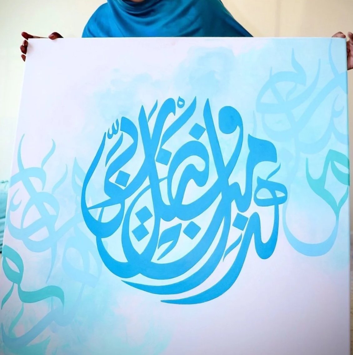 Person holding a large white canvas with blue Arabic calligraphy design.