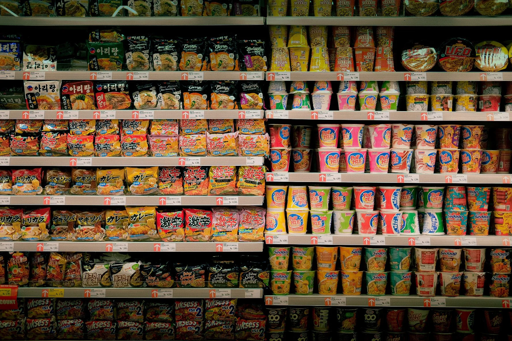 Shelves stocked with various instant noodles and cup soups in a grocery store.