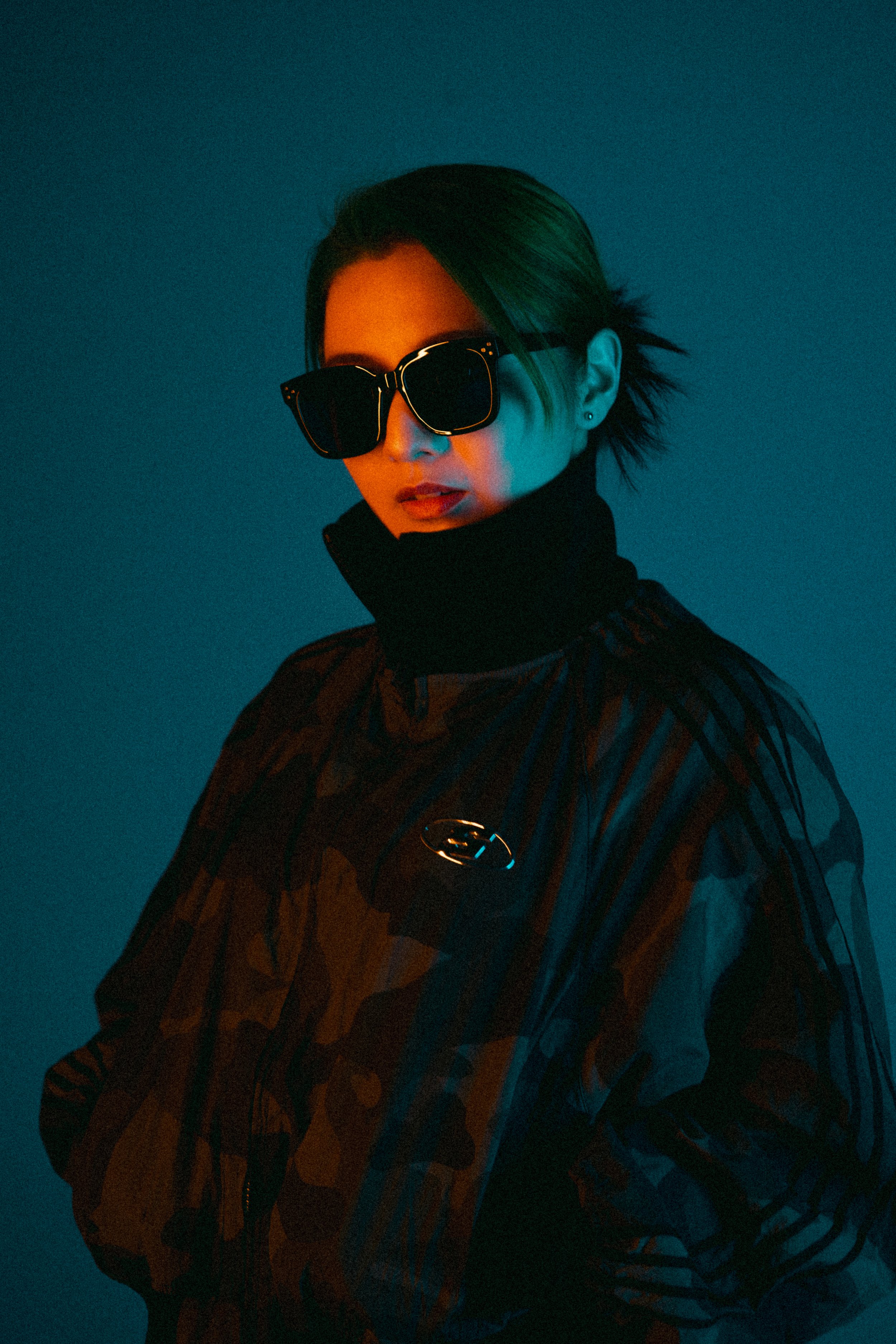 サングラスをかけた女性のポートレート、暗い背景に青とオレンジの照明。
