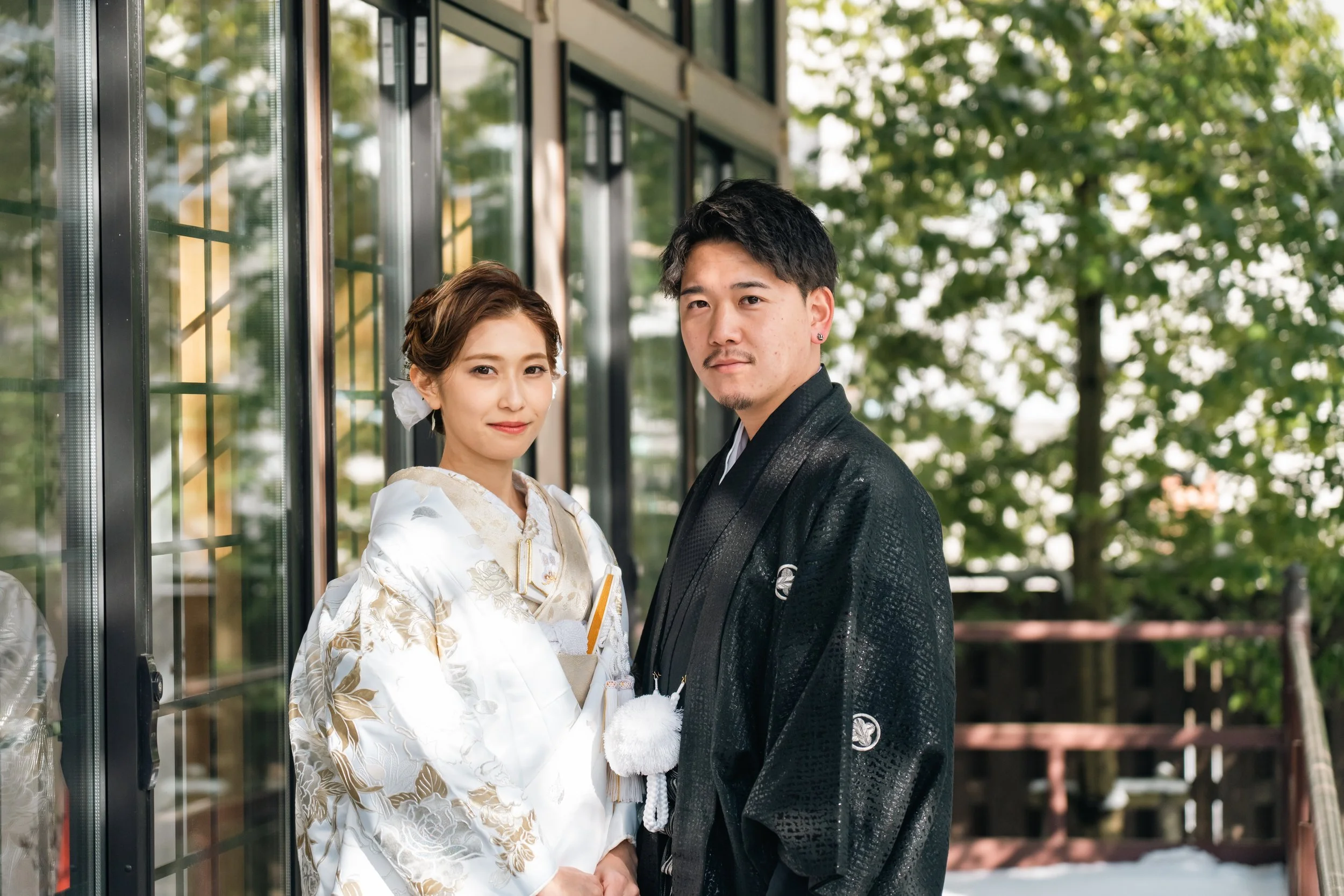 伝統的な和装を着た新郎新婦が外の自然の背景の前で並んで立っている写真