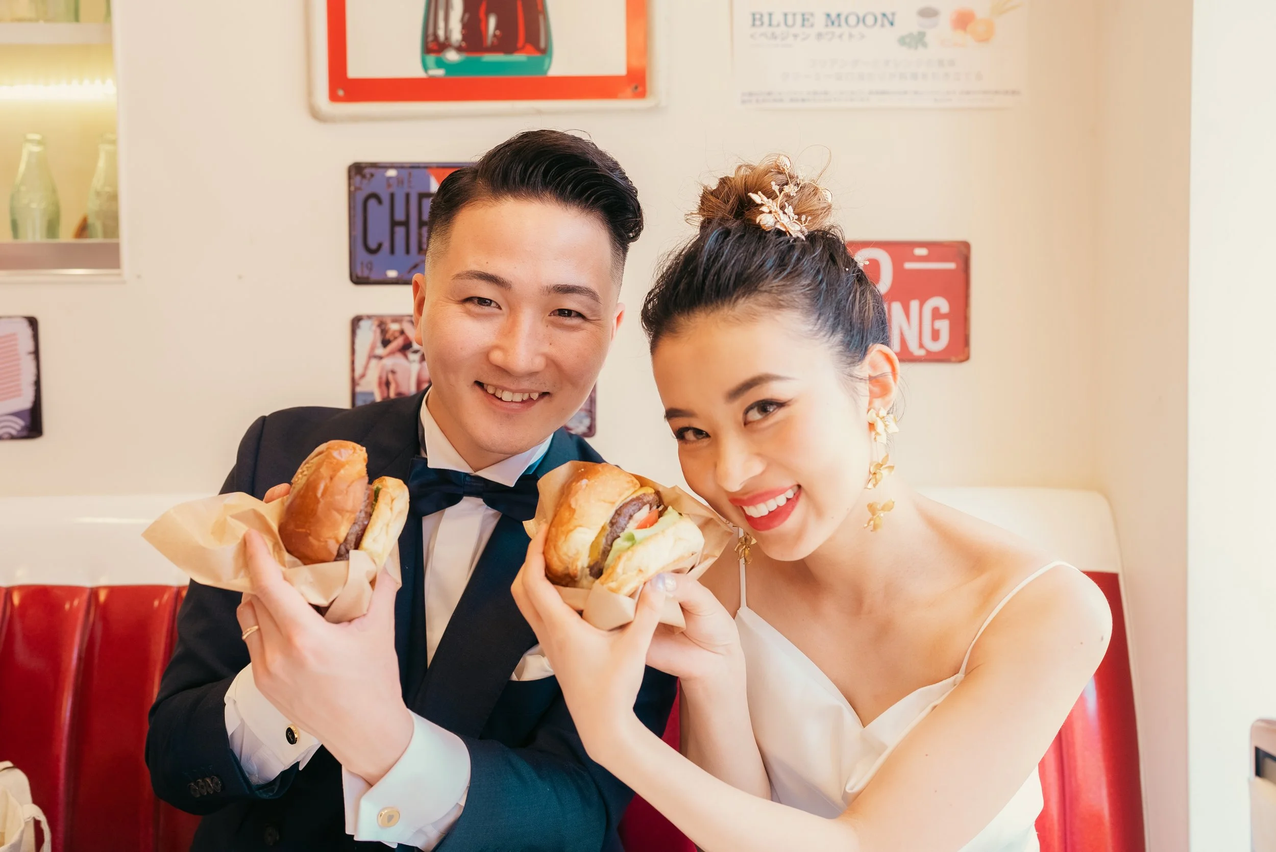 結婚式のドレスとスーツを着たカップルがレストランでハンバーガーを持ち笑顔で見つめている