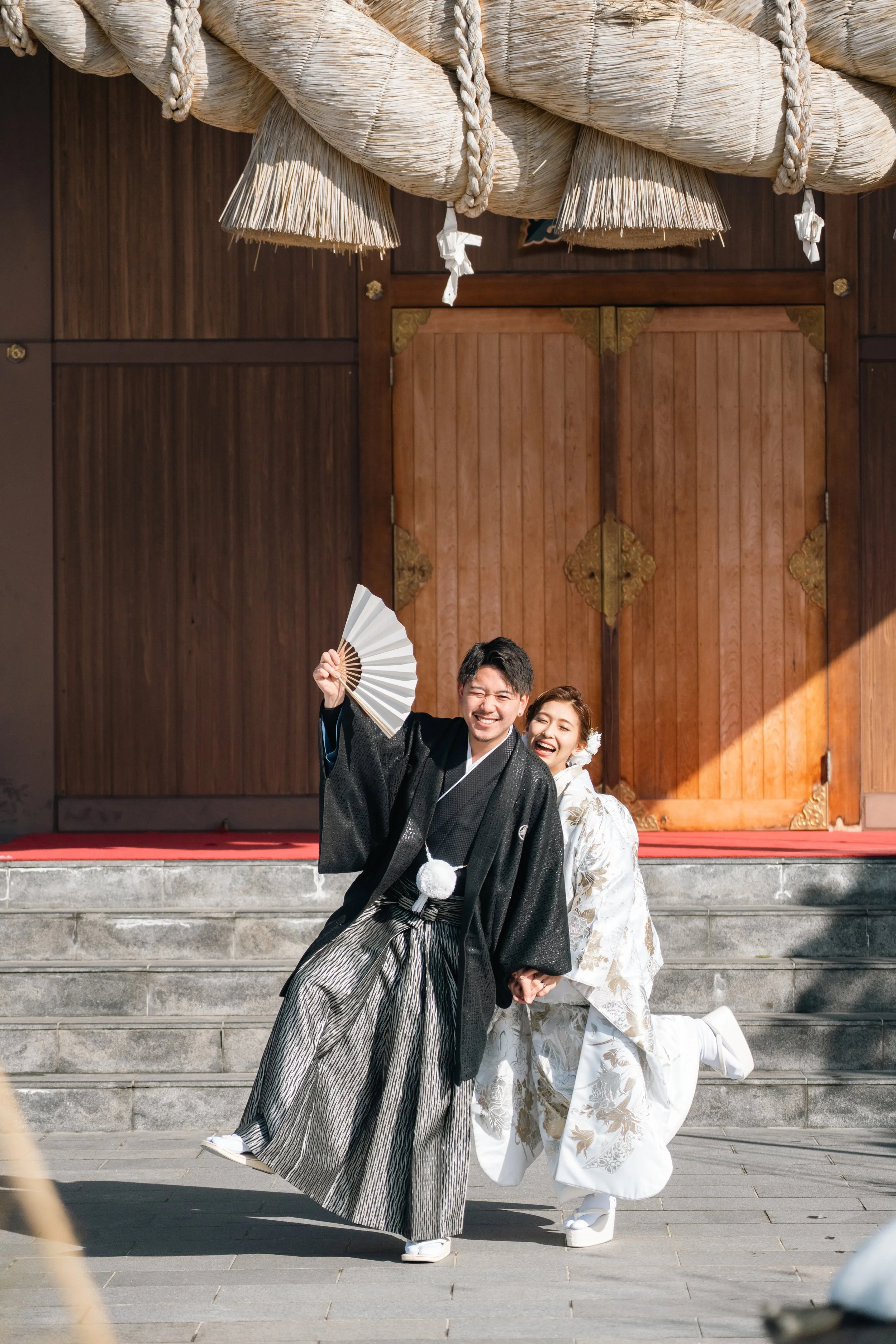 神社の前で着物を着た幸せそうな新郎新婦が笑顔でポーズをとっている写真