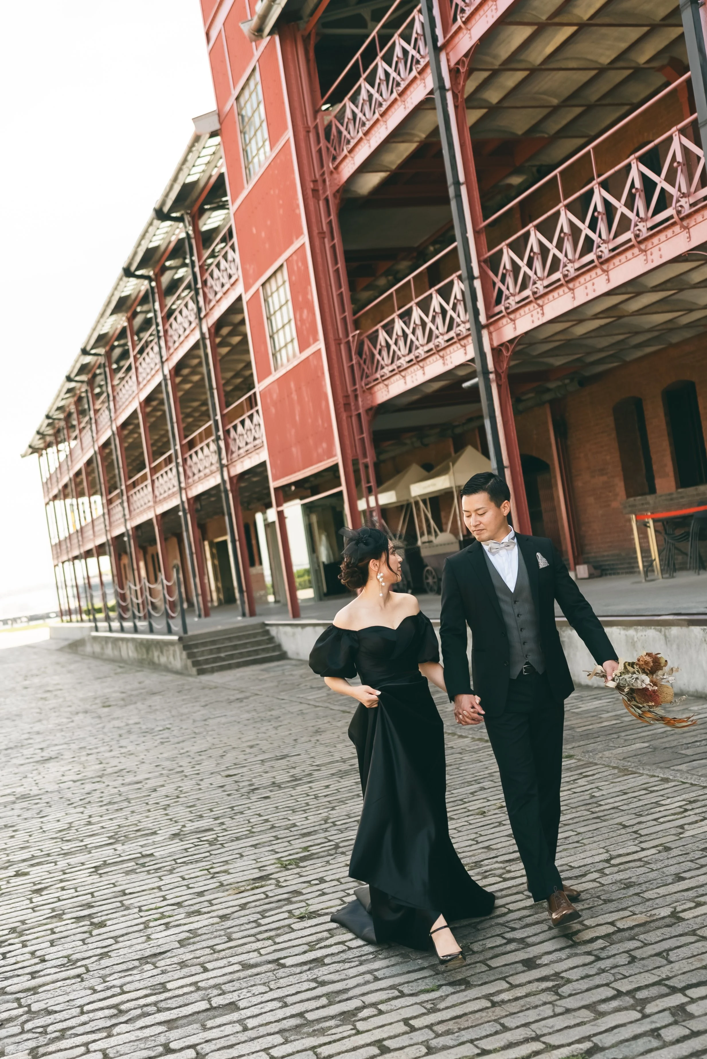 夜の街並みの中で手をつなぎ歩くウェディングドレスとスーツのカップルの写真