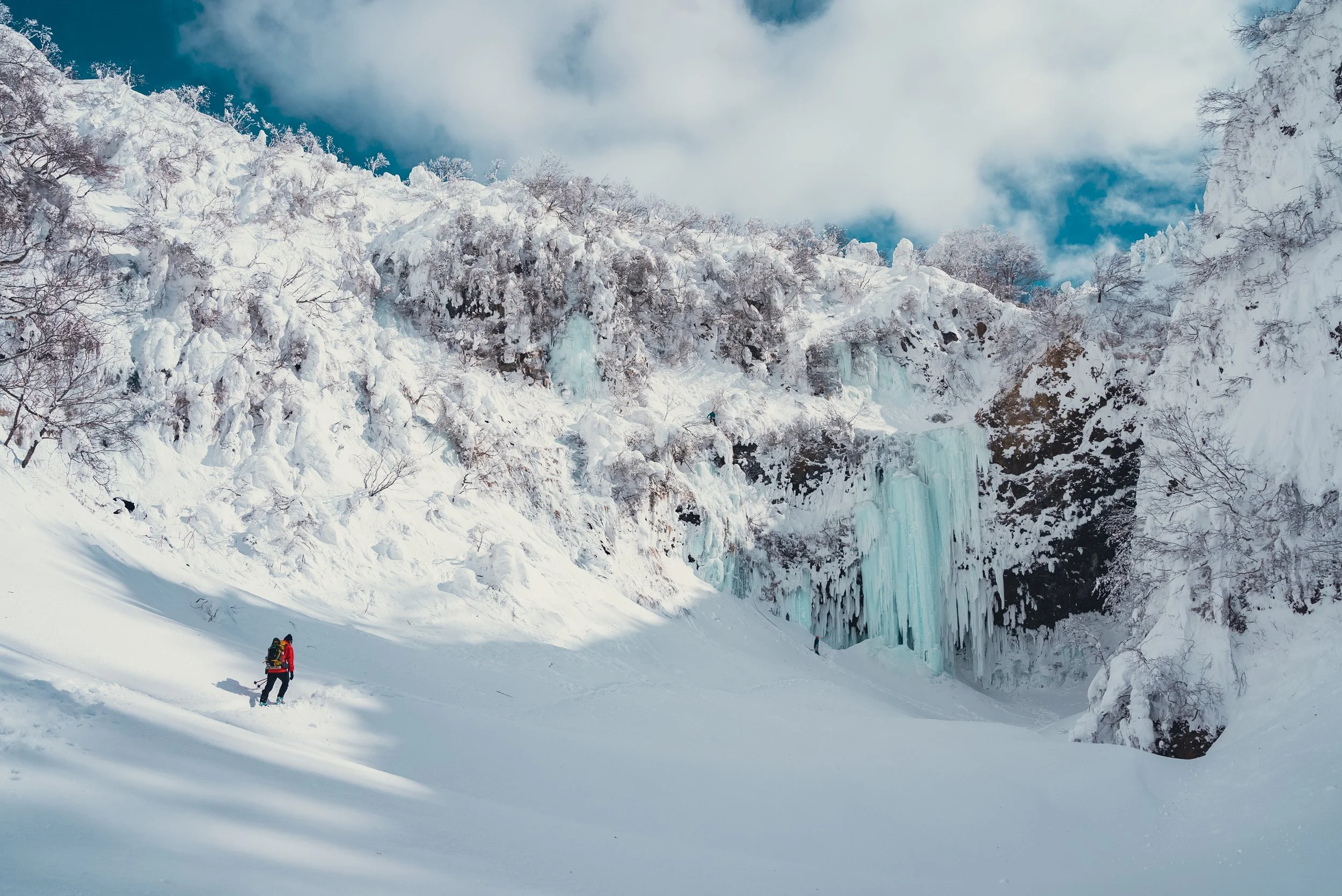 雪に覆われた山と氷柱、その中をスノーボードをした人たちが登っている風景