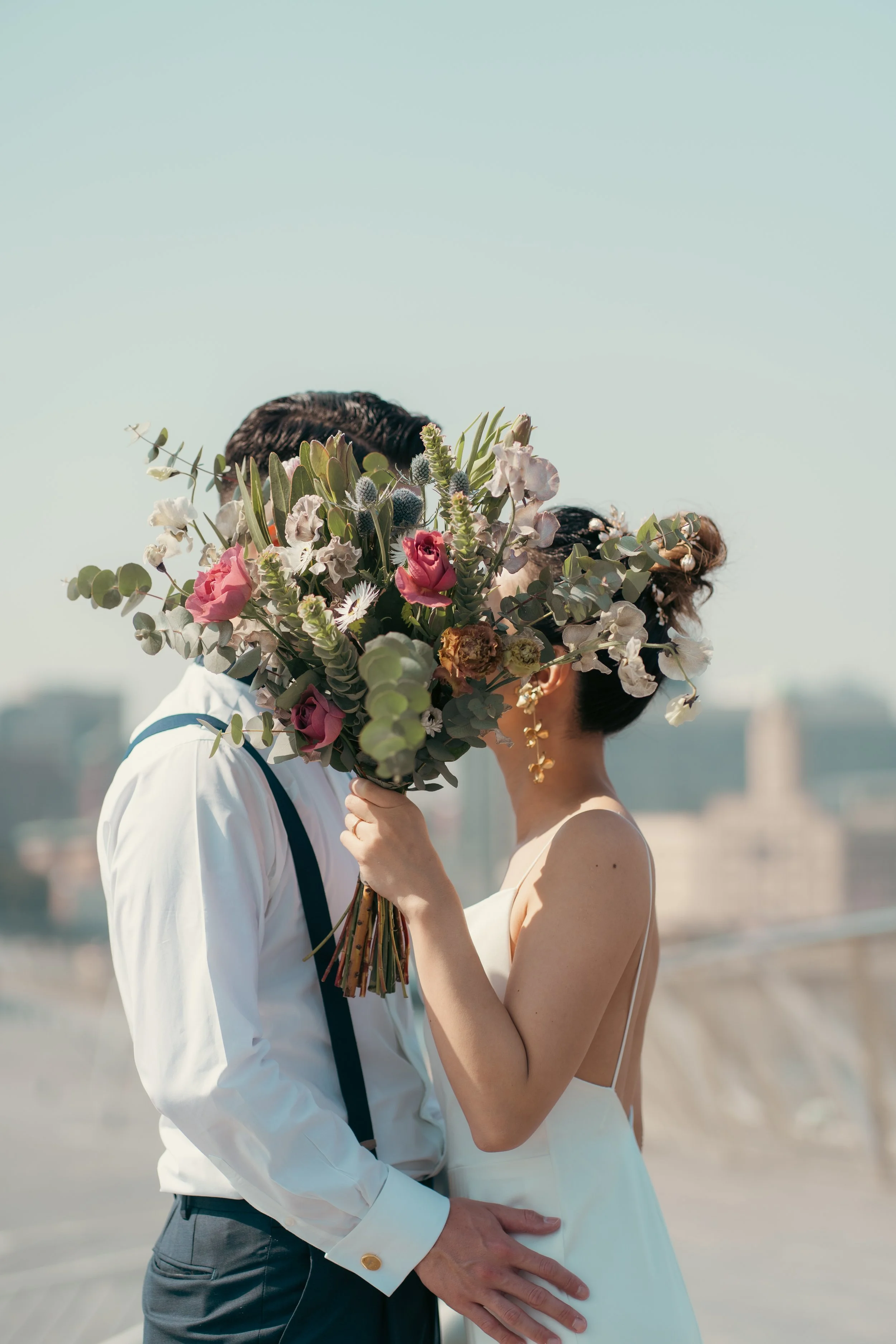 結婚した夫婦が屋上でキスしながら、女性は花束で顔を隠している写真