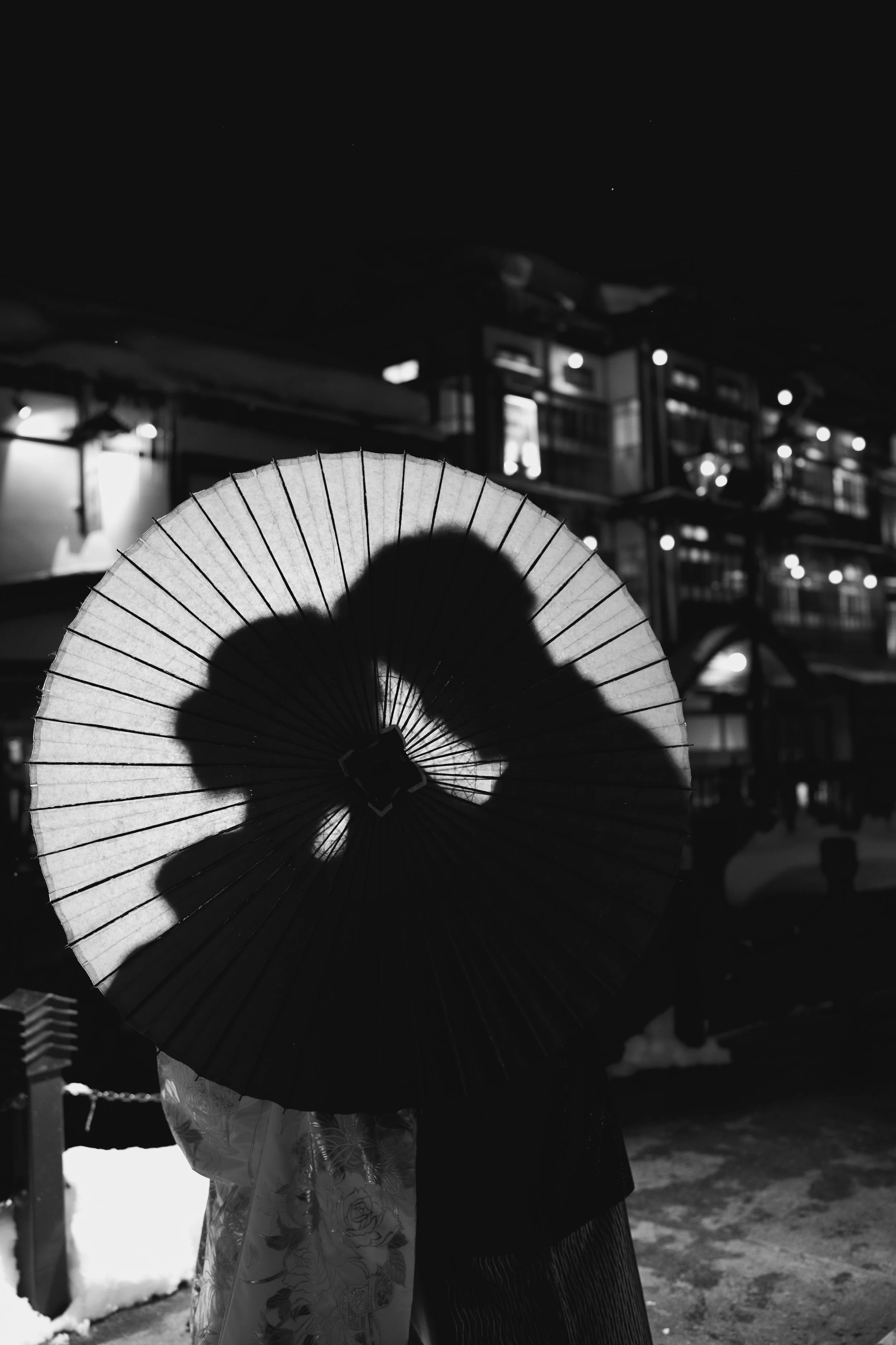 雪のある夜の街で、傘をさす二人のシルエット。