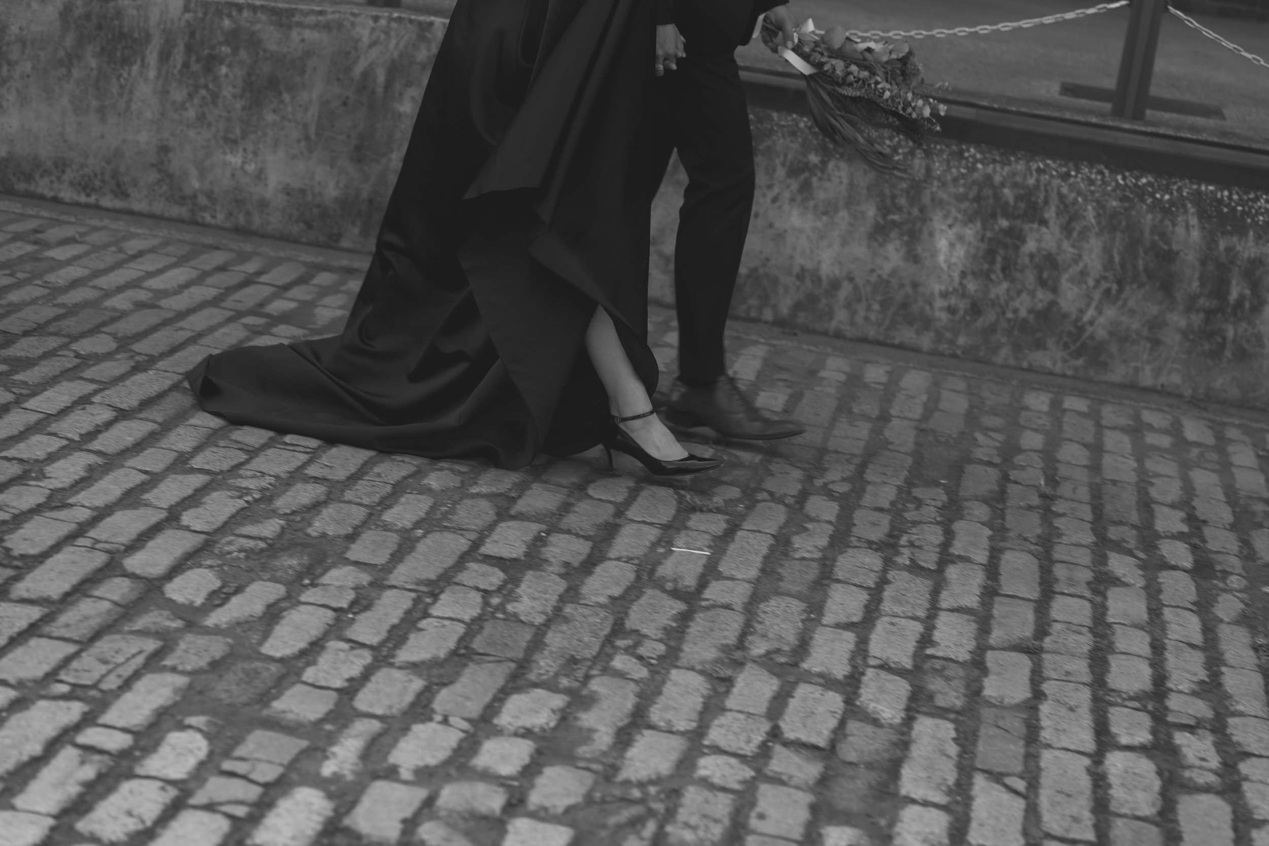 結婚式の会場前で、新郎と新婦の足元が写された写真。新婦はハイヒールを履き、ドレスの裾を持ち上げている。