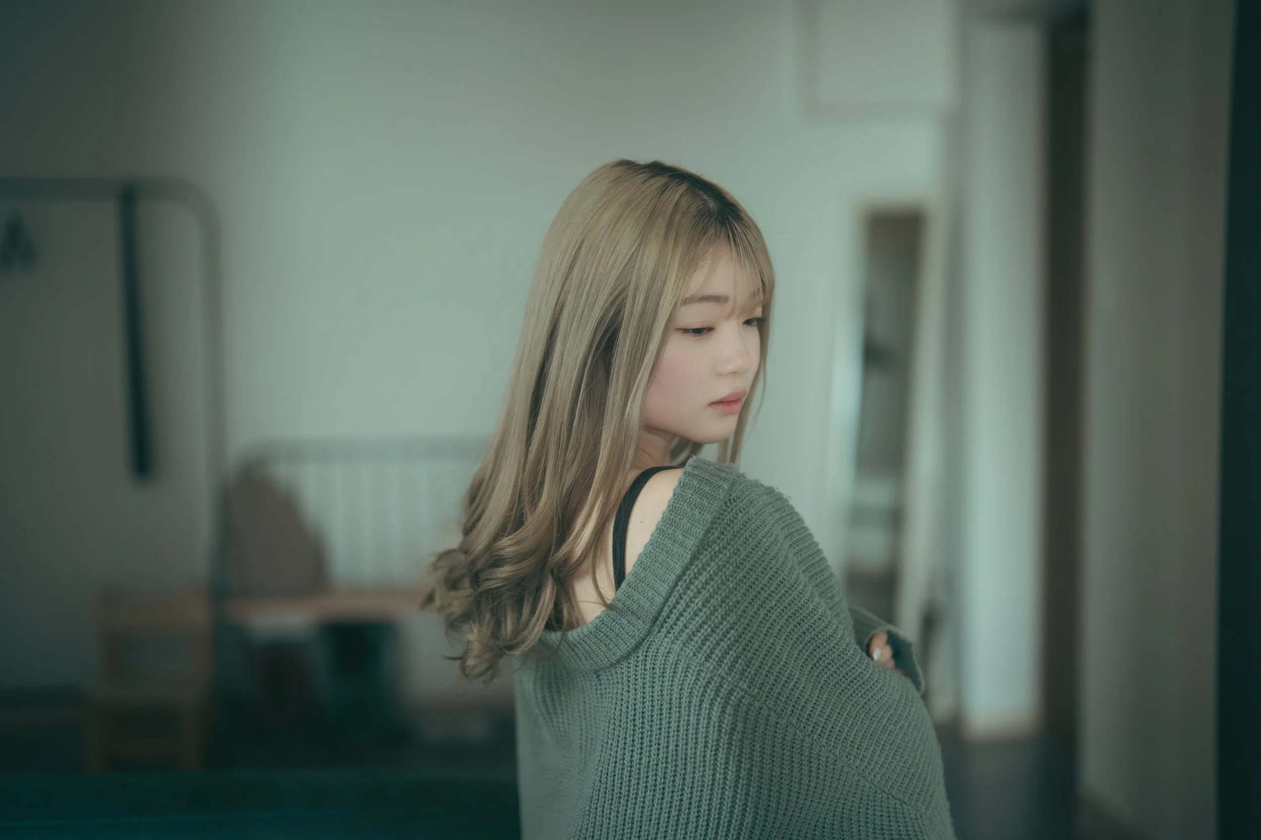 灰色のセーターを着た若い女性が窓のほうを見ている。