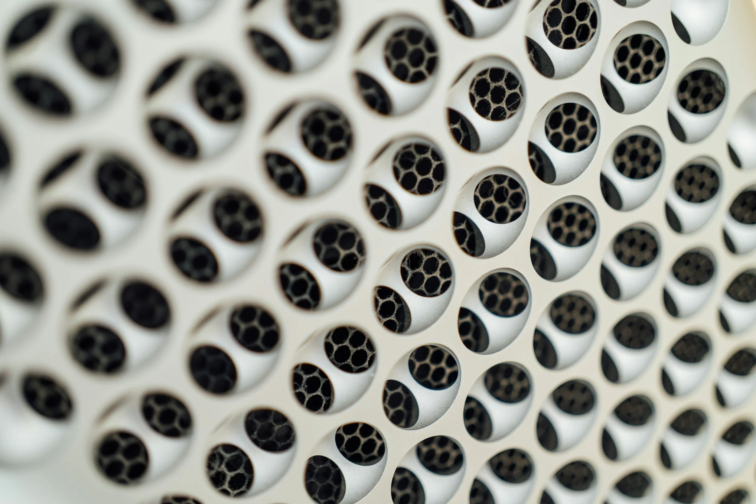 Close-up of a white metallic surface with a pattern of circular holes, revealing inner black tubes.
