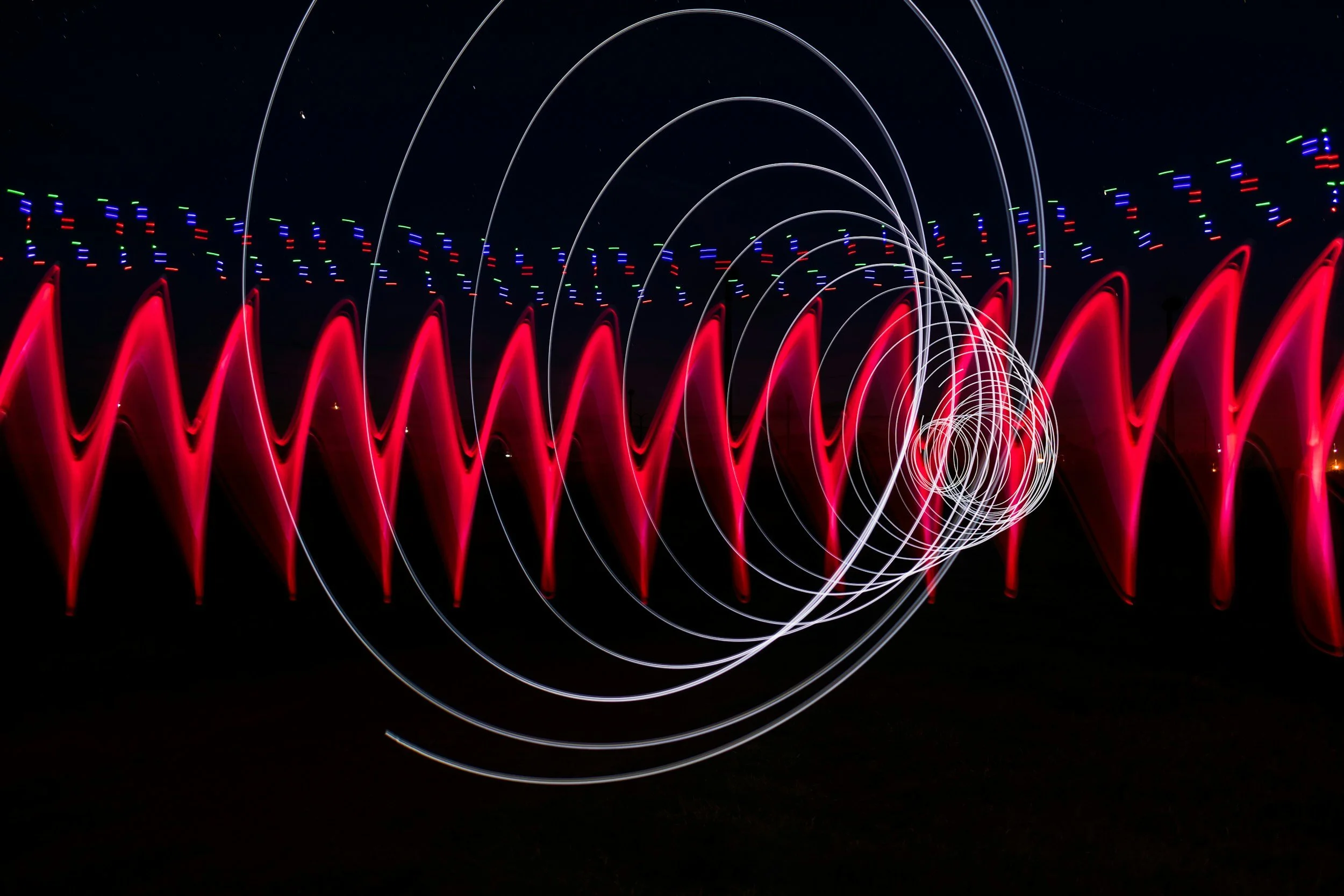 Light painting at night with red, white, green, and blue light trails creating abstract organic shapes and patterns.