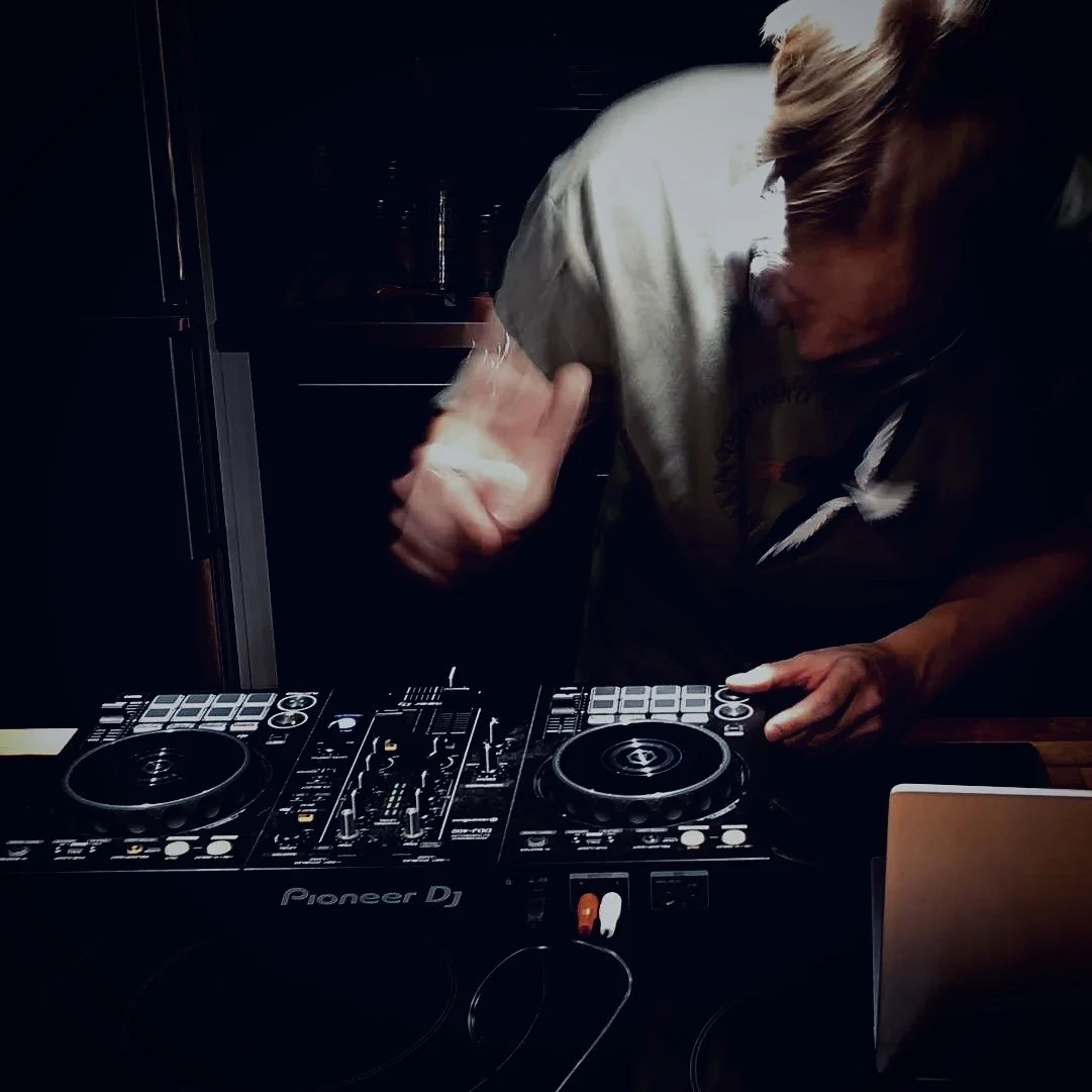 A person DJing using Pioneer DJ equipment, with their right hand on the mixer and their head tilted downward in a dark environment.
