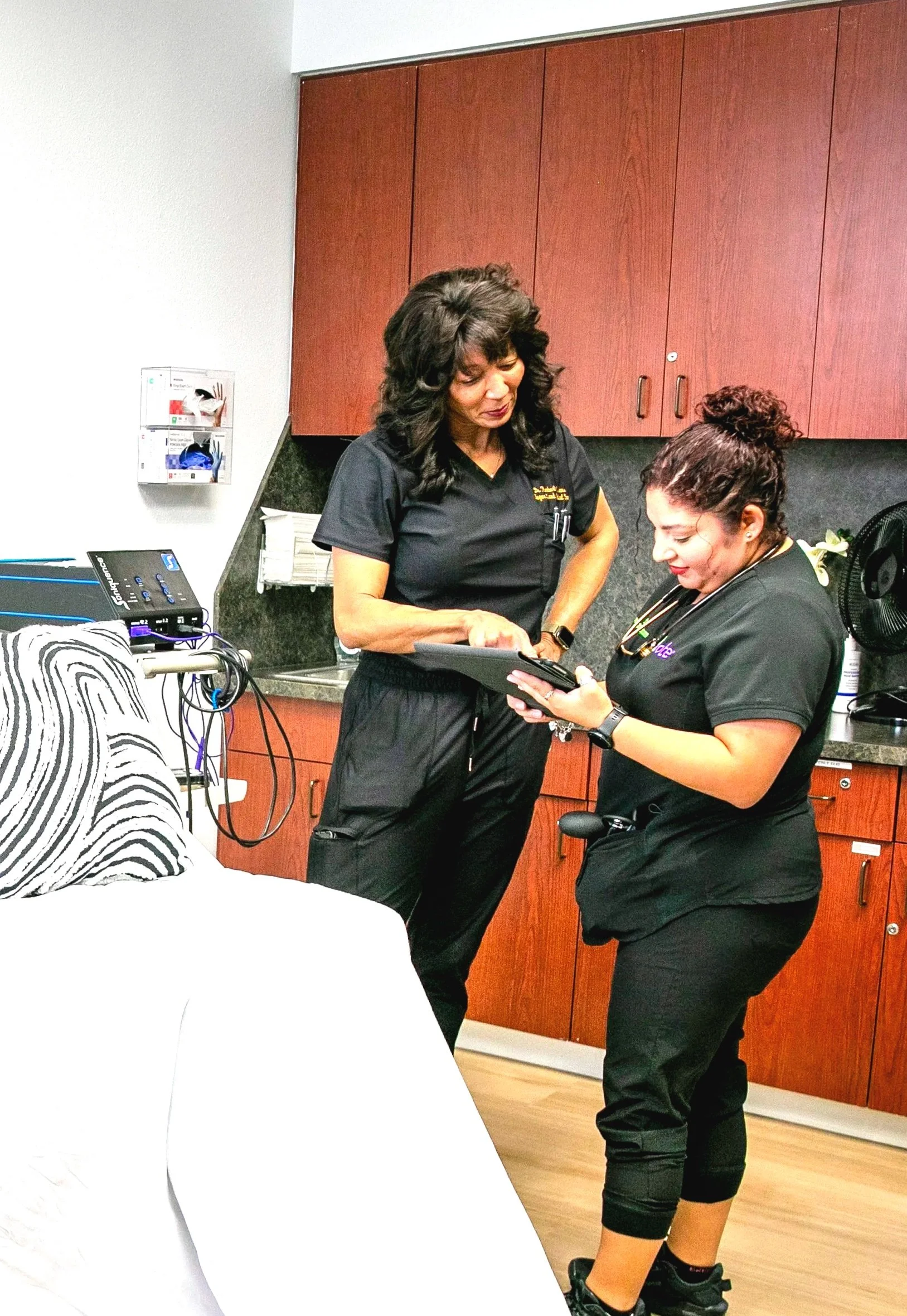 Two healthcare professionals standing in a medical setting, looking at a tablet device together.