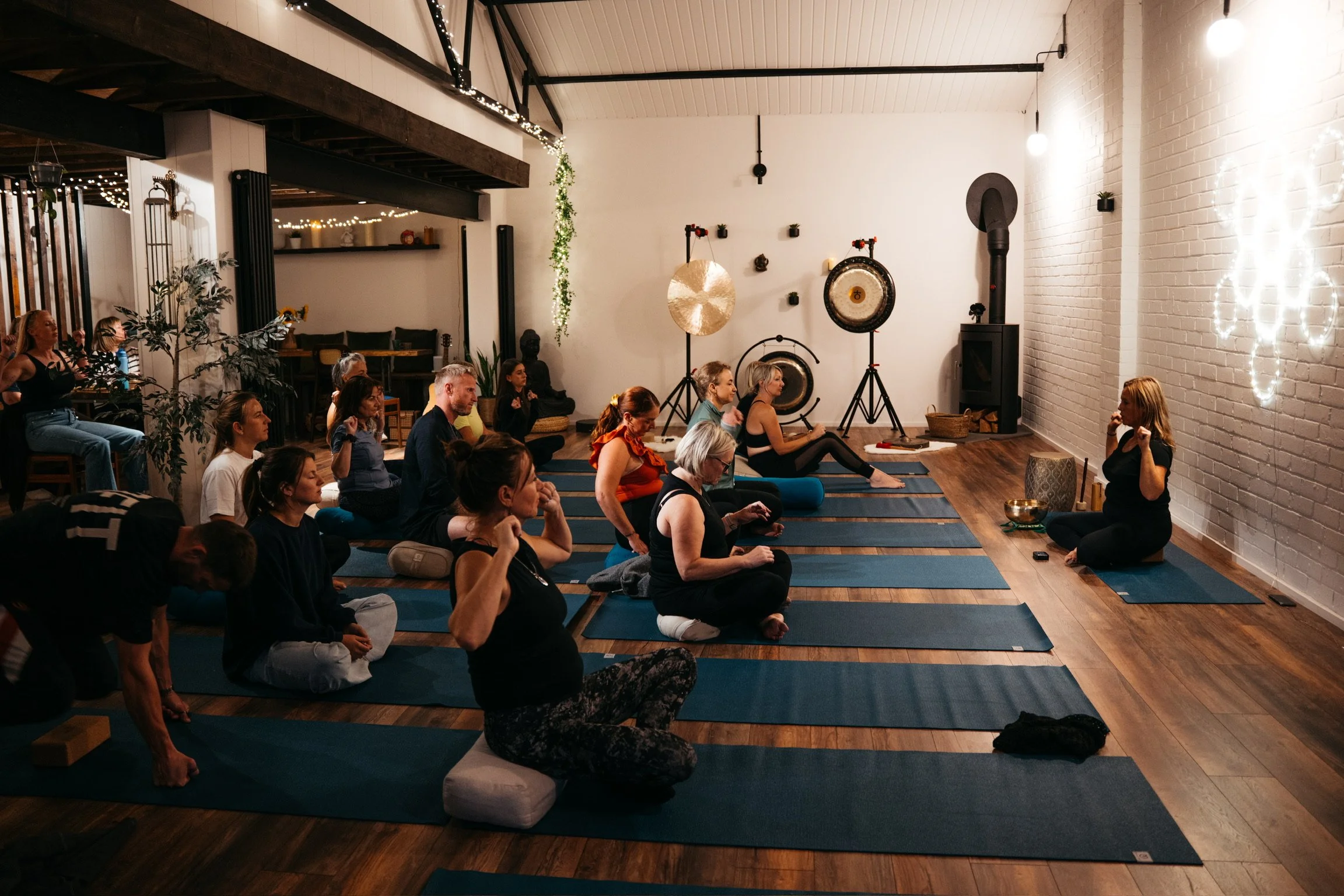People participating in a yoga or meditation class in a cozy, well-decorated studio with musical instruments and soft lighting.