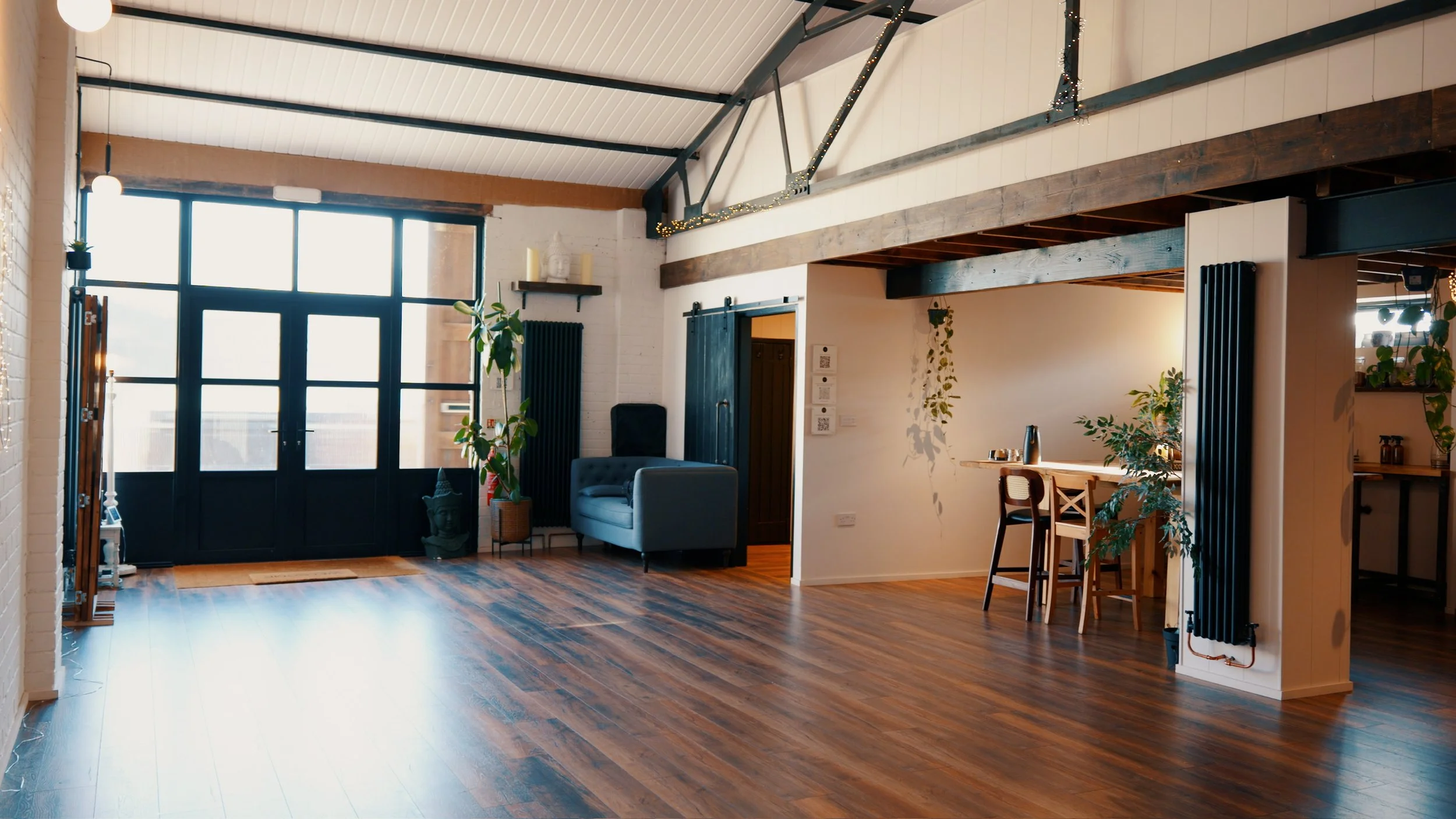 Spacious living area with large front door, hardwood floors, a light blue armchair, indoor plants, and a bar-height dining area.