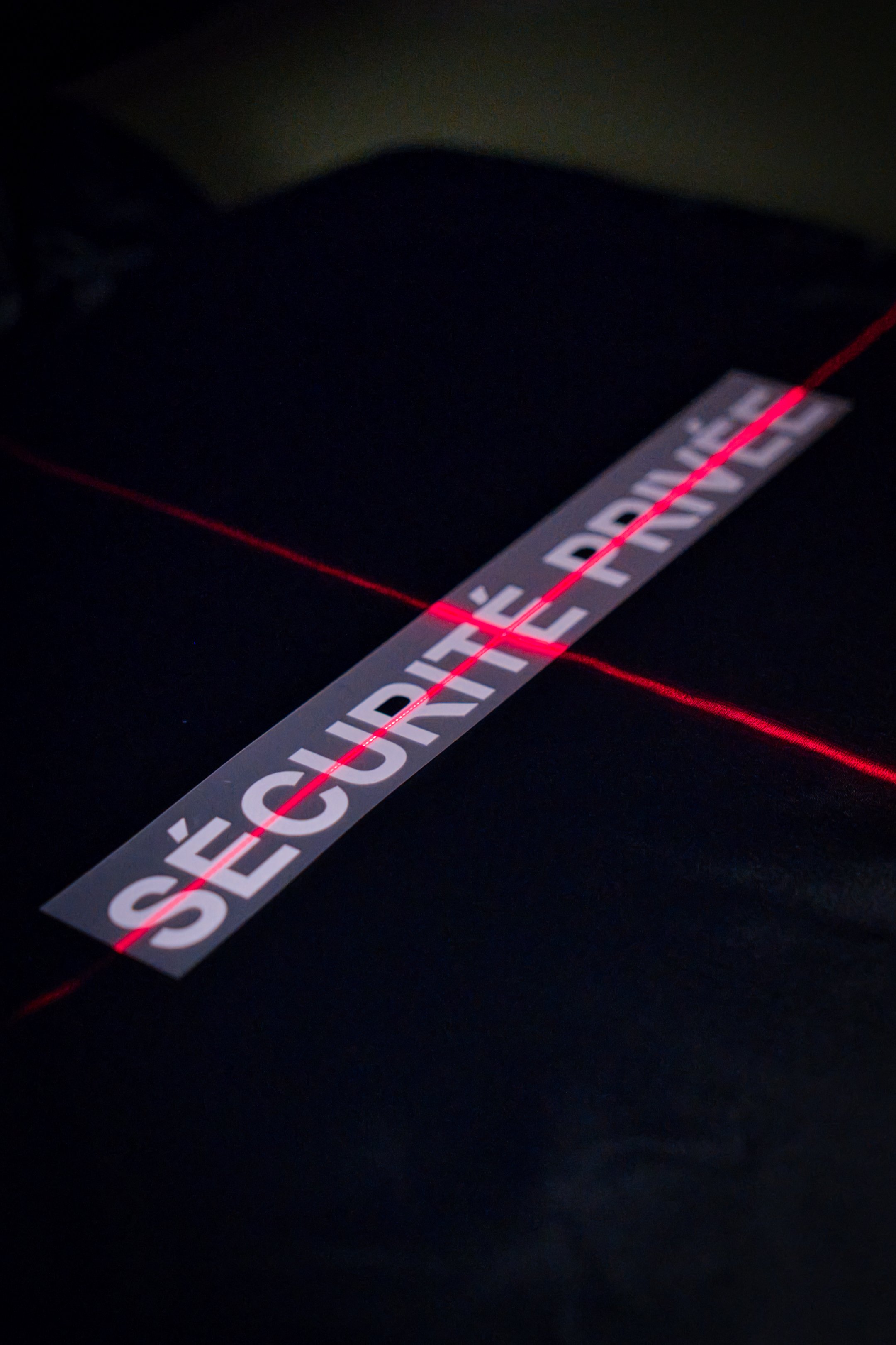 Une bande adhésive avec l'inscription 'SÉCURITÉ PRÉCAUTIONS' en blanc, traversée par un faisceau laser rouge.