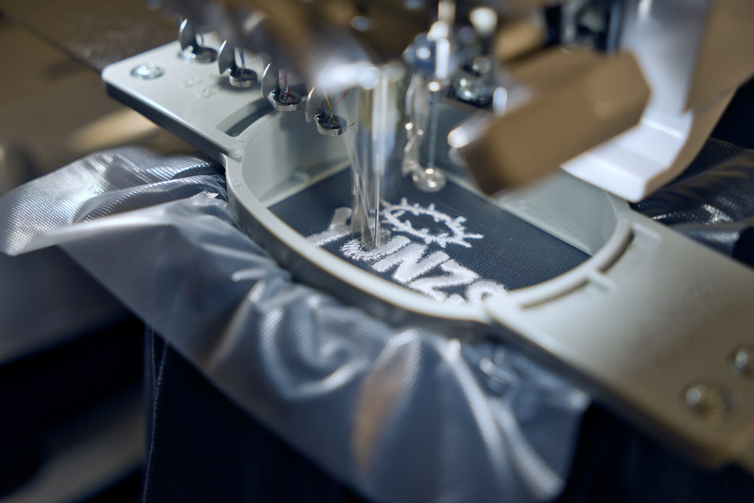Une machine de broderie en action créant un logo blanc sur un tissu noir.