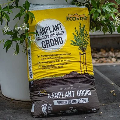 Zakje met aarde en een jonge plant, bestemd voor het groeien van eetbare planten, met tekst in het Nederlands over de voordelen van de grond.