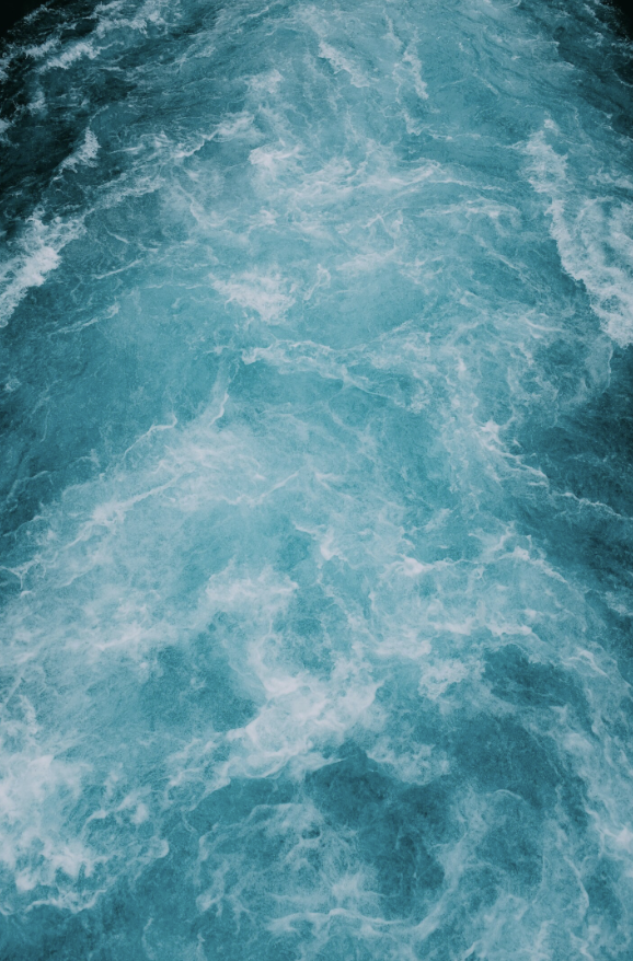 Aerial view of turbulent, deep blue ocean water with white foam.