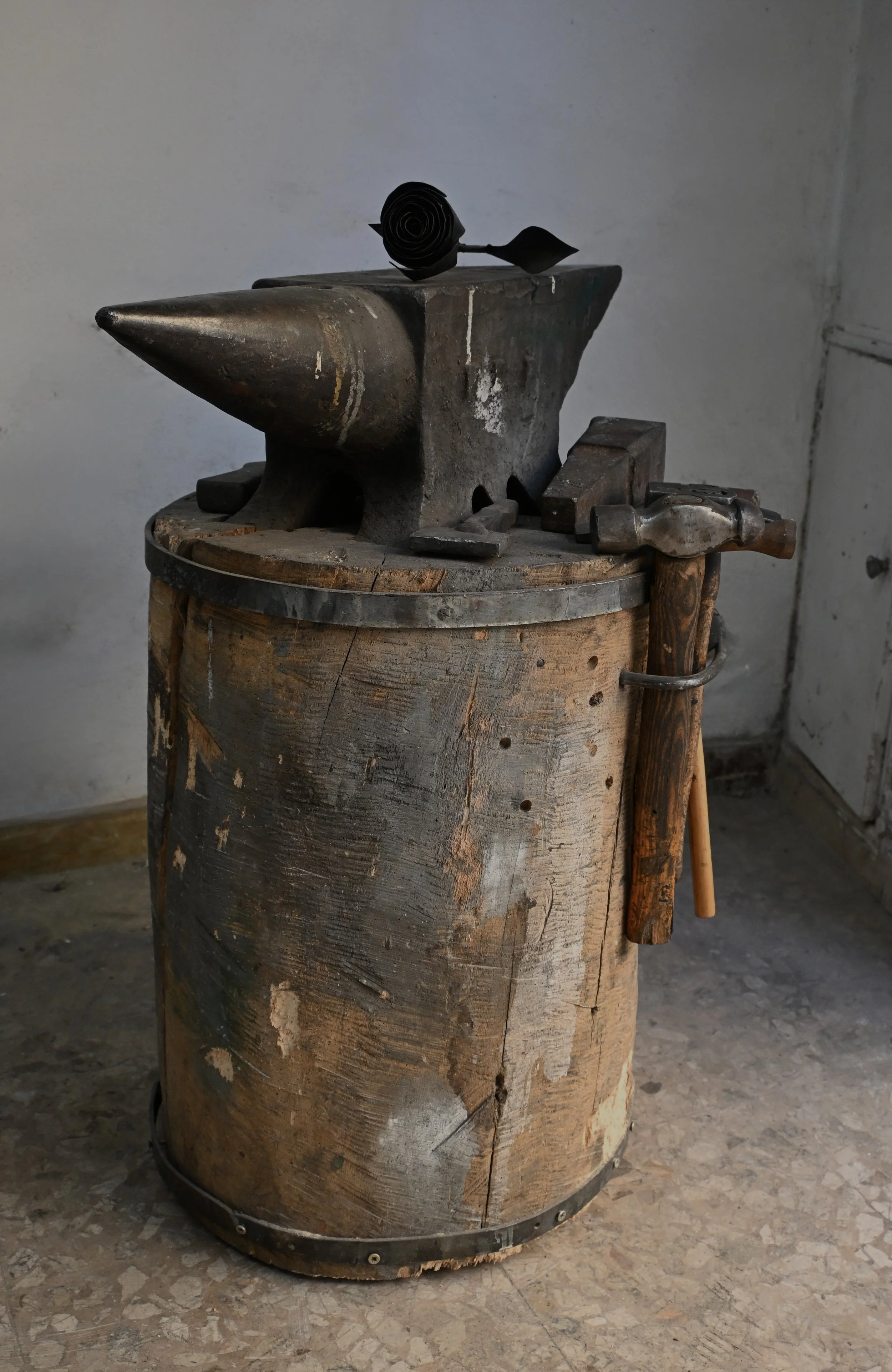 Un tavolo in legno con un'incudine e un martello, usato per la lavorazione del metallo, con un fiore nero sopra.