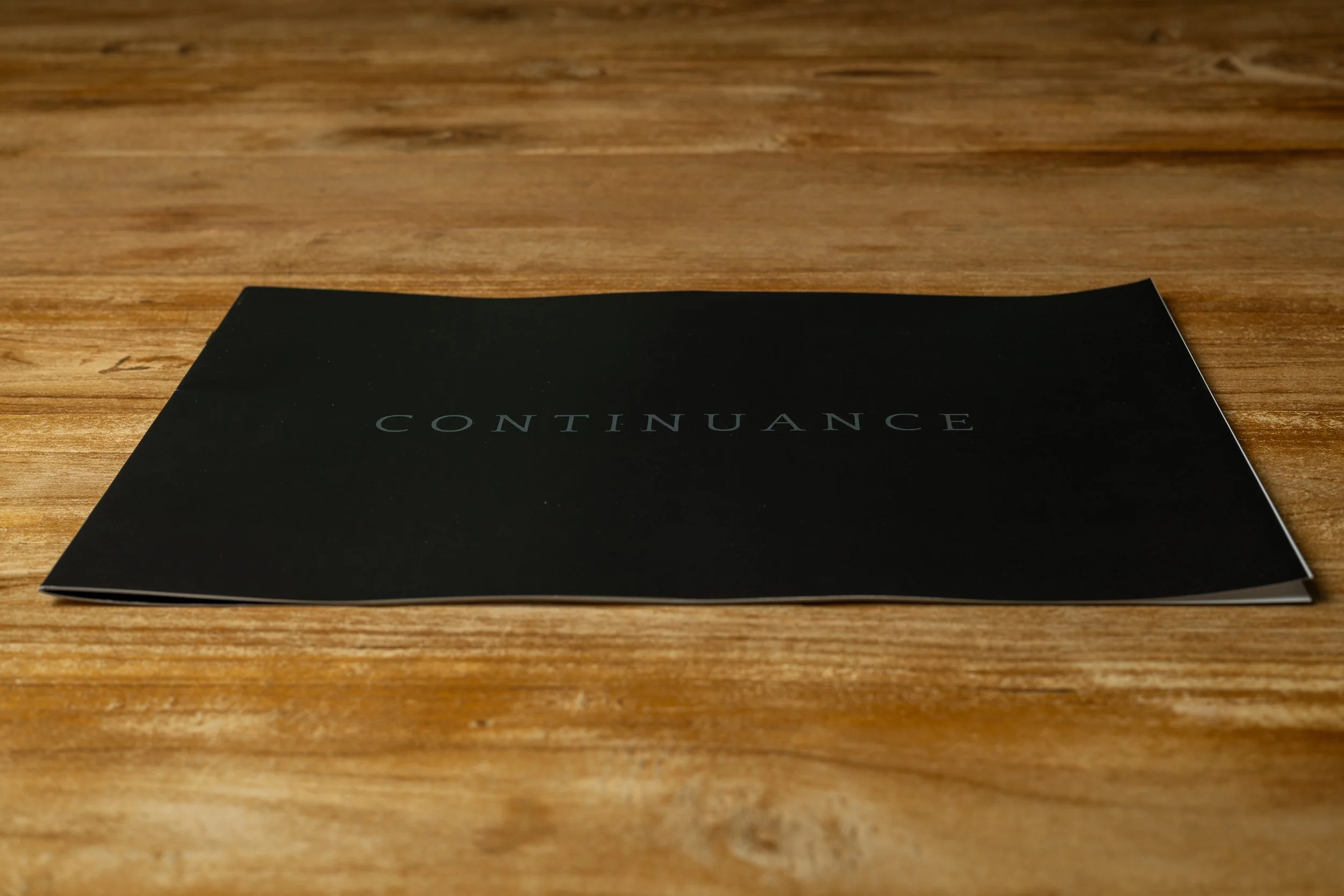 Photo booklet “Continuance” on a wooden surface, angled view