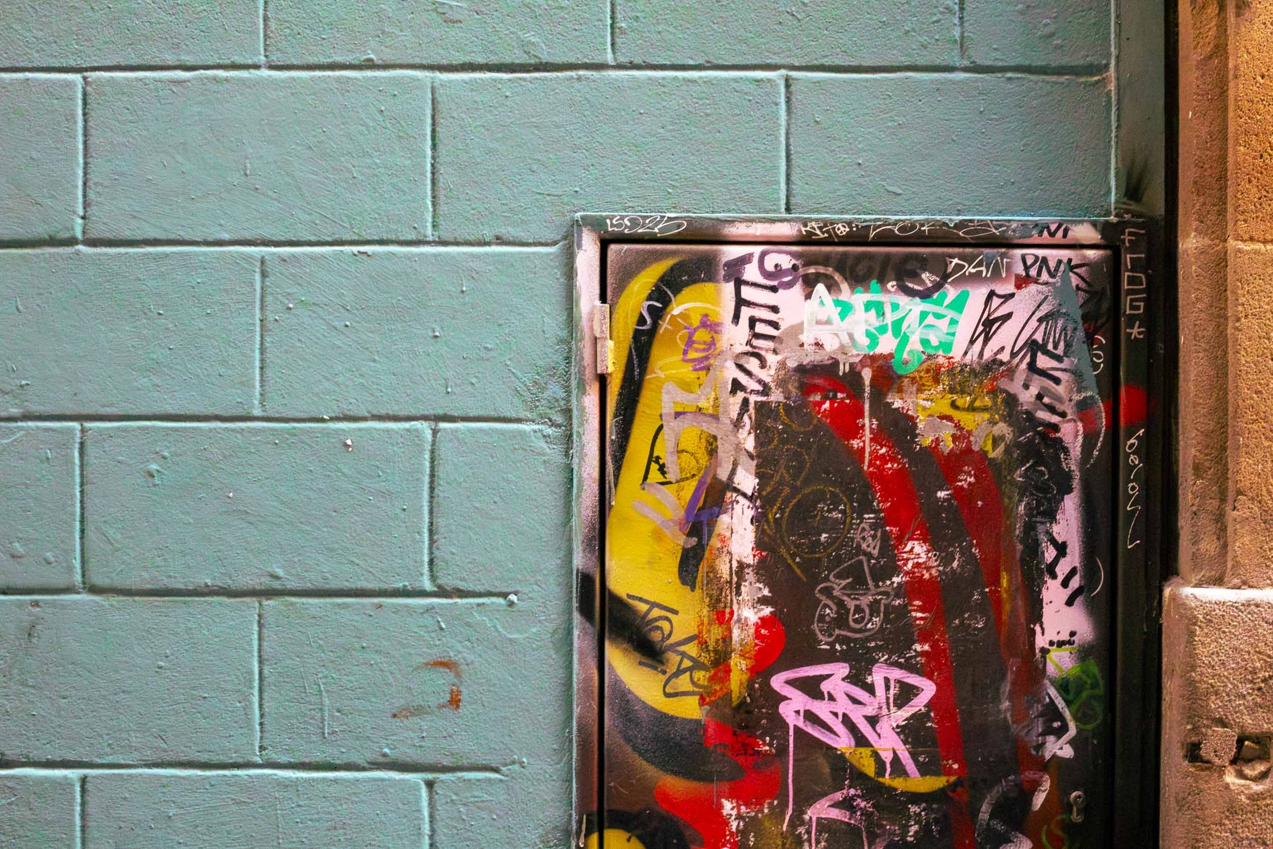 Graffiti-covered metal door in a turquoise brick wall in the Gothic Quarter of Barcelona.