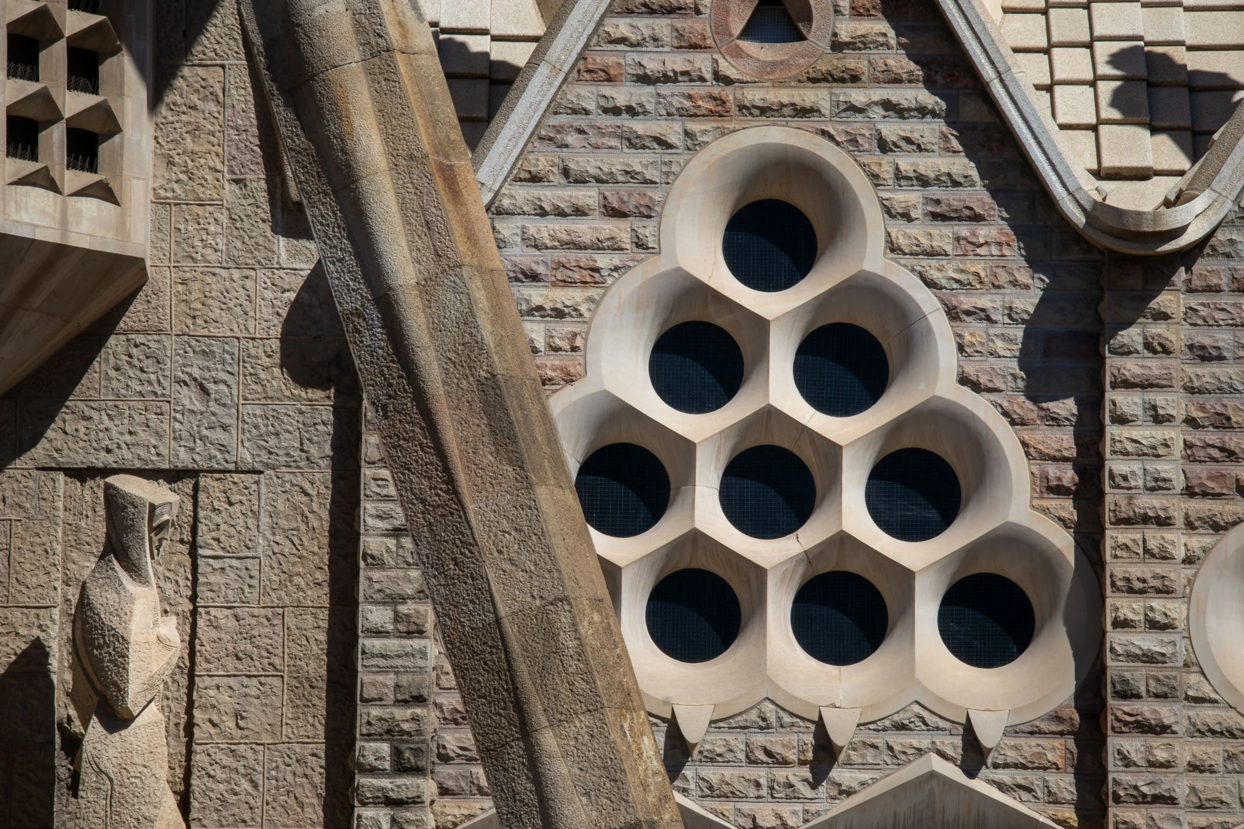 Geometric stone window detail on the facade of La Sagrada Família in Barcelona, with circular openings set into textured stone walls and intersecting structural elements.