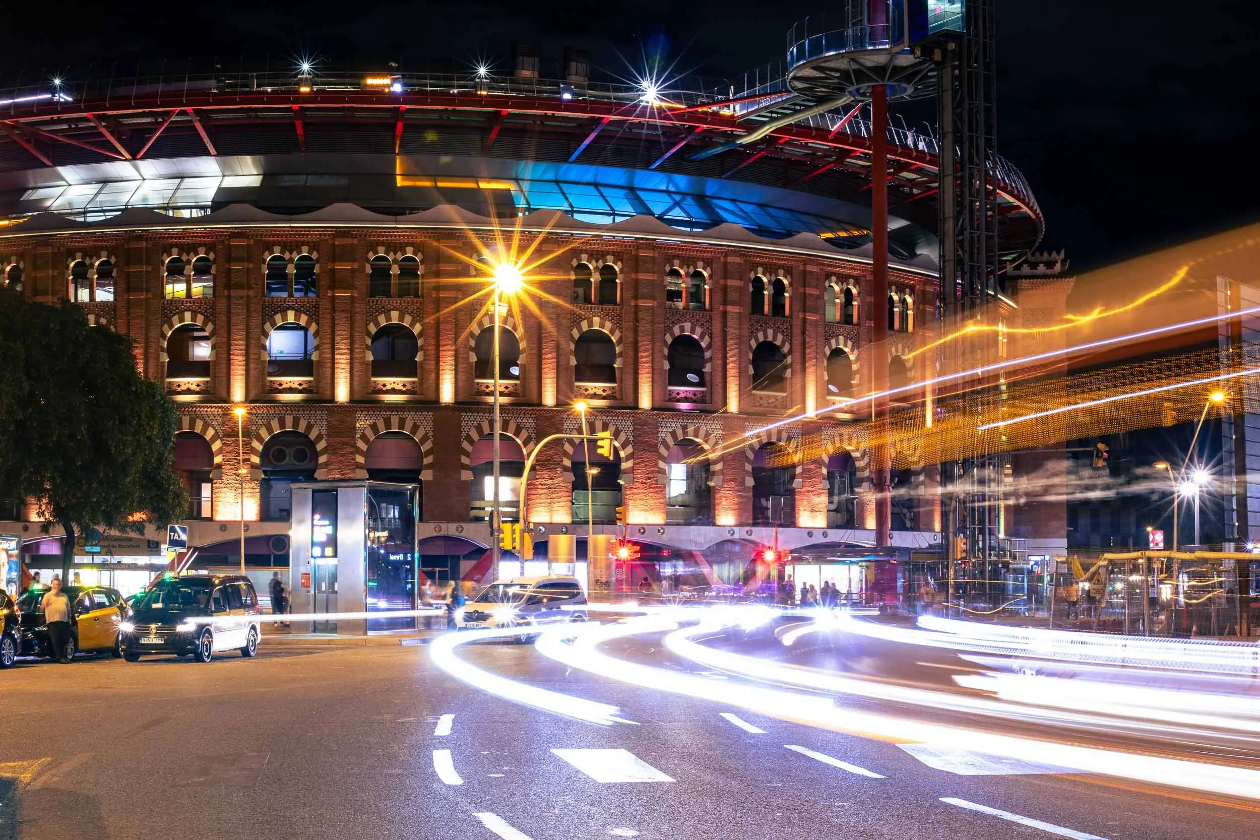 Night view of Plaça d’Espanya in Barcelona with the circular Arenas building and light trails from passing traffic.