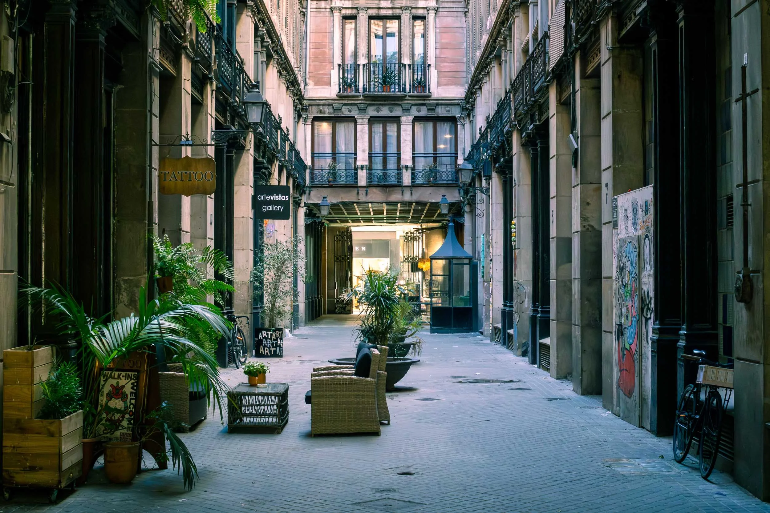 arrow alley in the Gothic Quarter of Barcelona with historic buildings, balconies, and potted plants.
