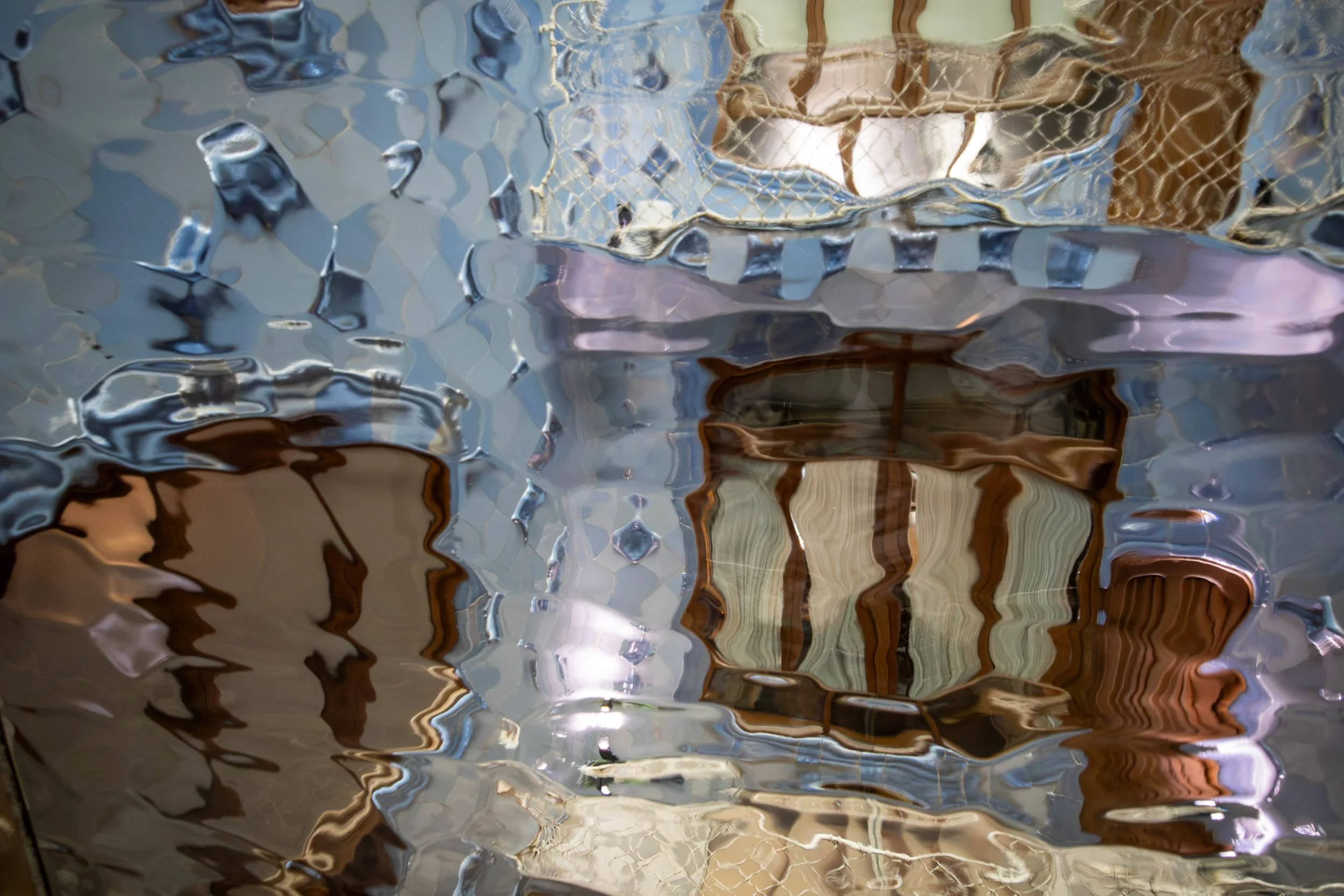 Abstract view of textured glass inside Casa Batlló in Barcelona, distorting reflections of interior shapes, colors, and architectural details.