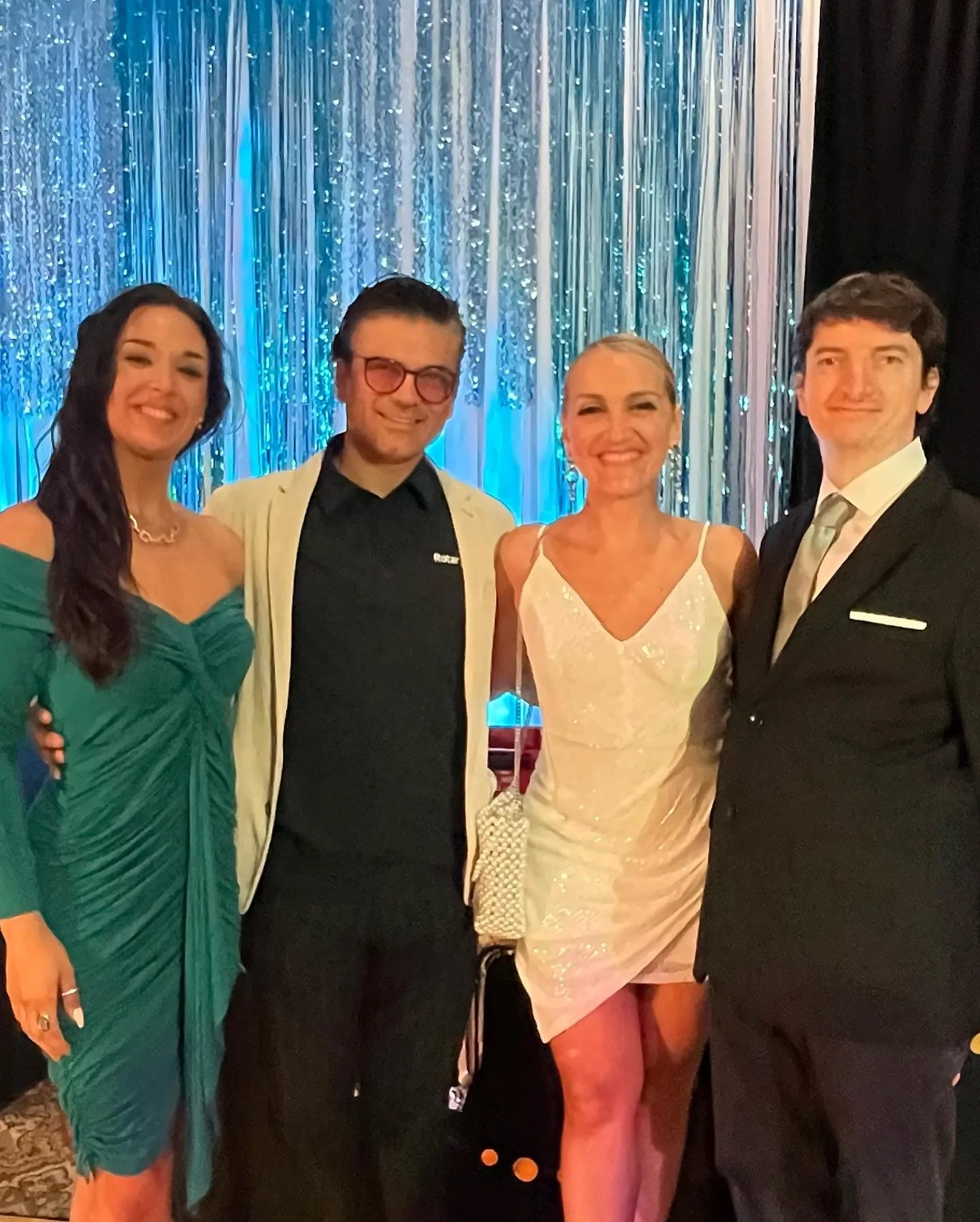 Four people dressed in formal attire posing together at an event with a blue and silver shimmering backdrop.