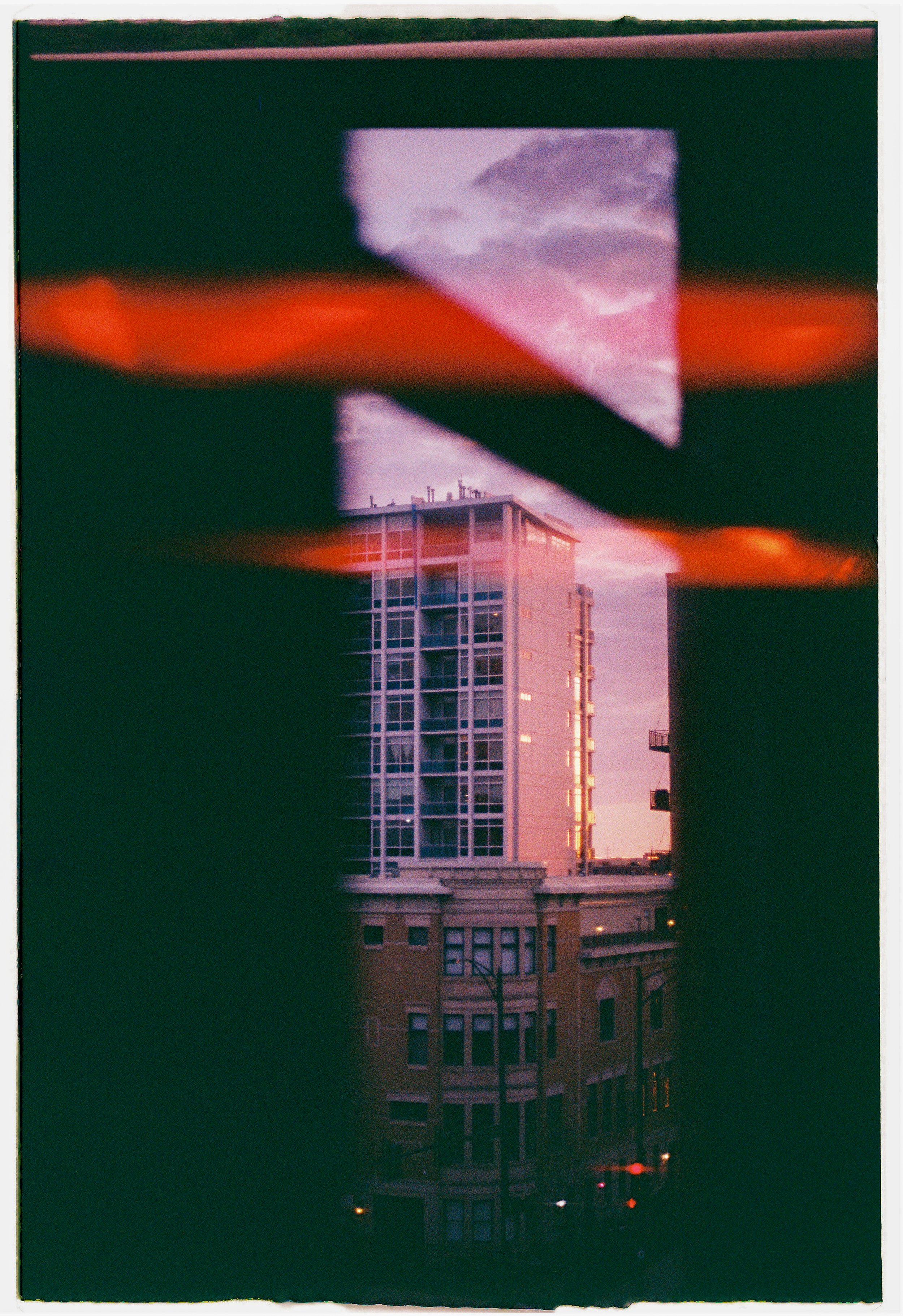 Urban cityscape view through a peephole in a door or window, showing a tall building and a sunset sky.