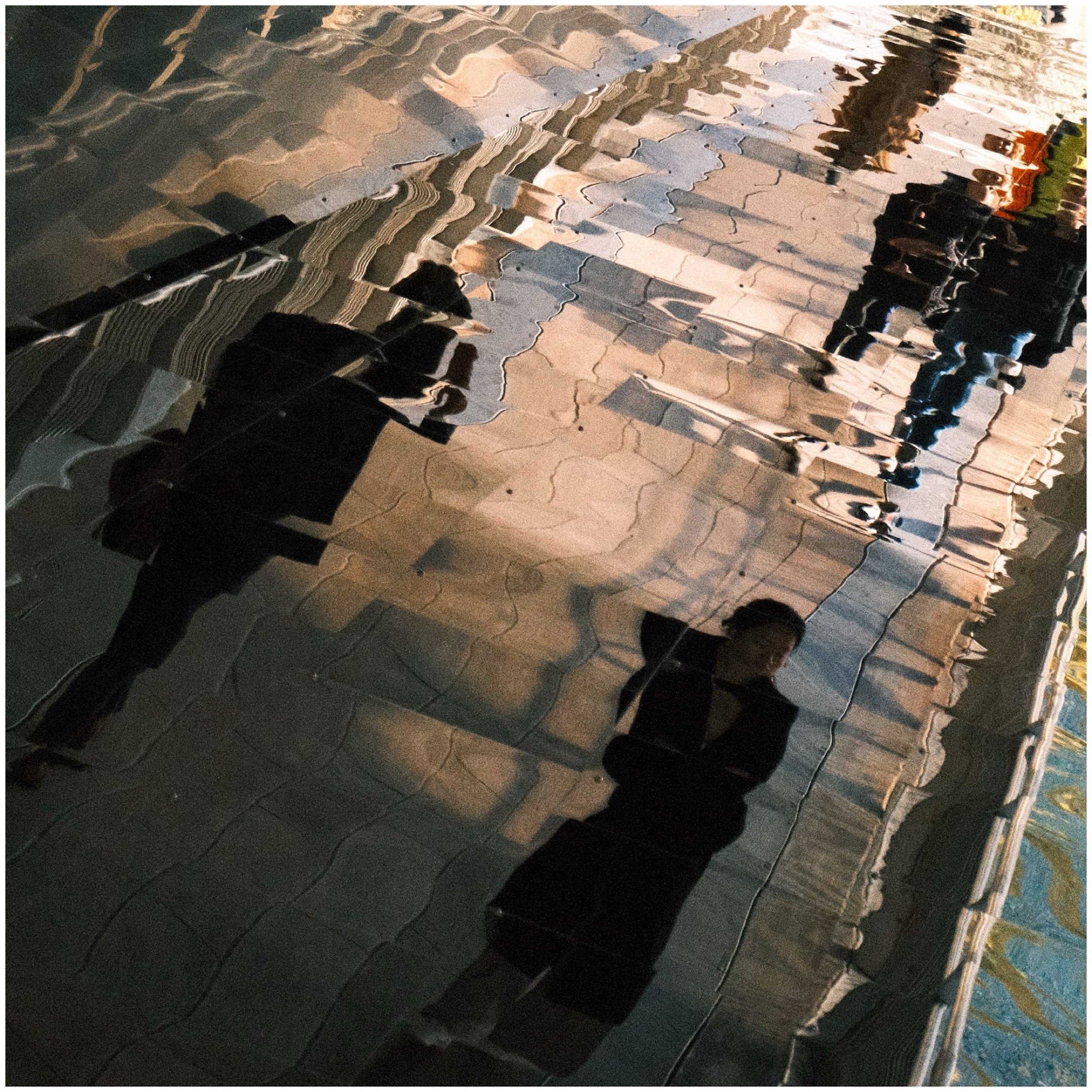 Reflections of people and architecture in a shiny, wavy metallic surface.